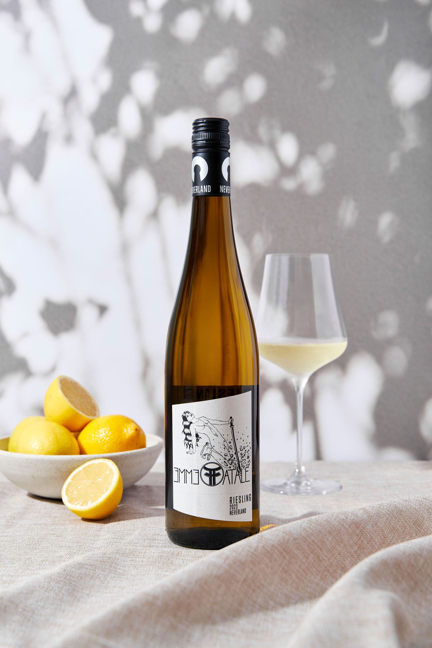 Riesling white wine bottle beside a full glass and fresh lemons on a linen cloth.