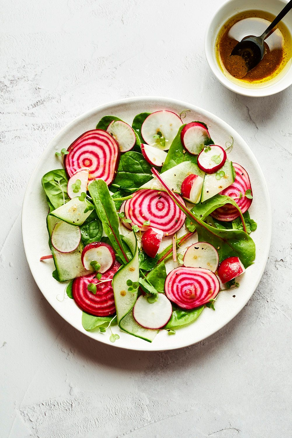 Fresh radish salad with cucumber ribbons, striped beets, and vinaigrette dressing on white plate.