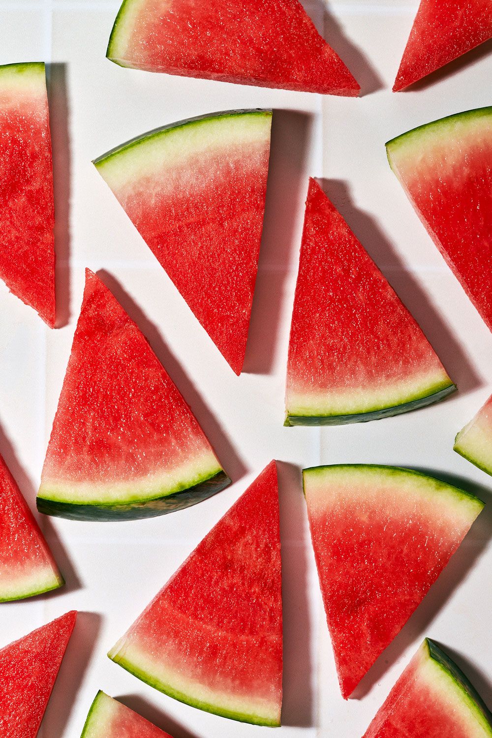 Fresh watermelon slices arranged on white background, showing vibrant red flesh and green rind.