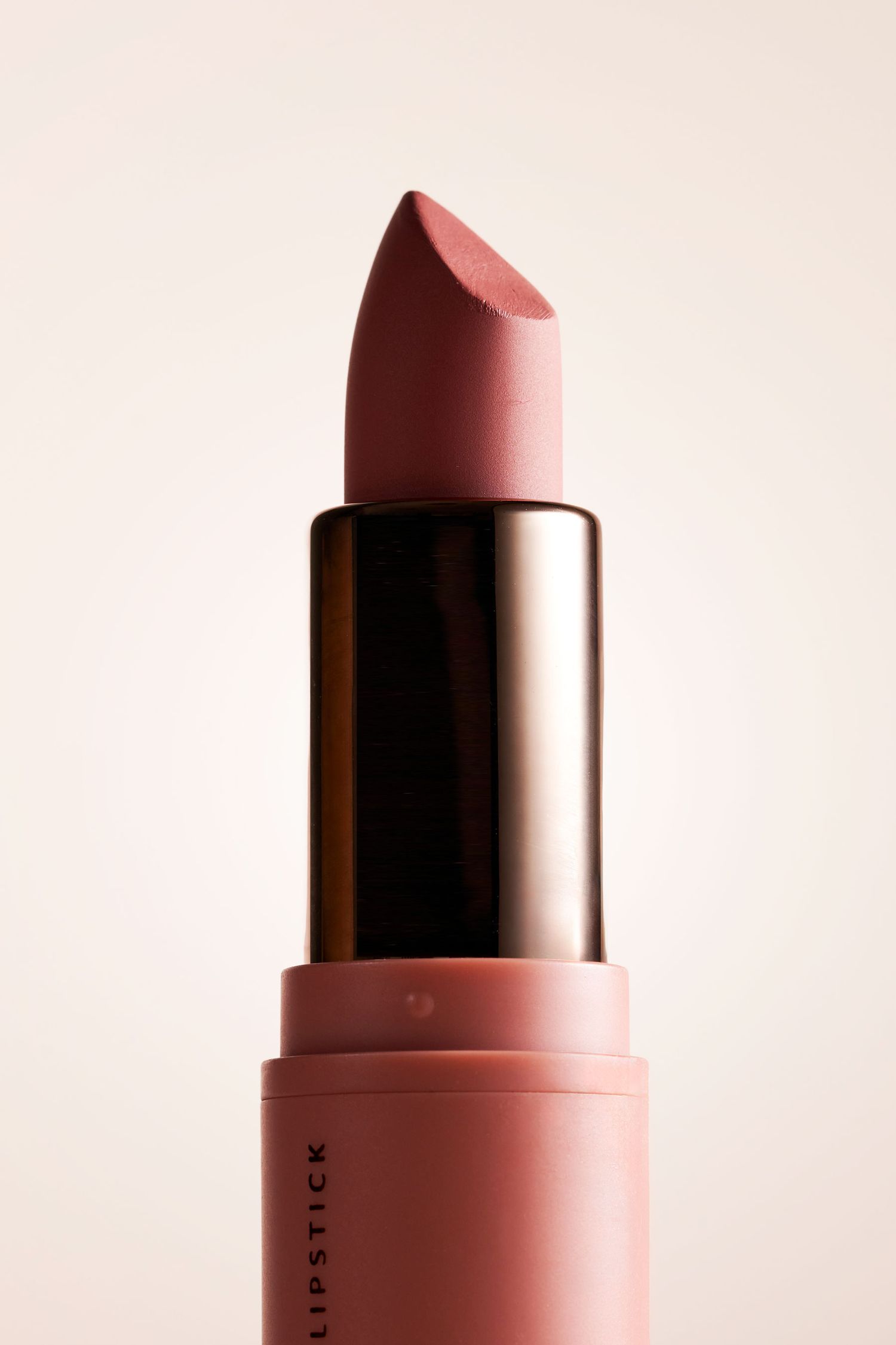 Close-up of an open dusty rose matte lipstick bullet with gold metal casing on neutral background.