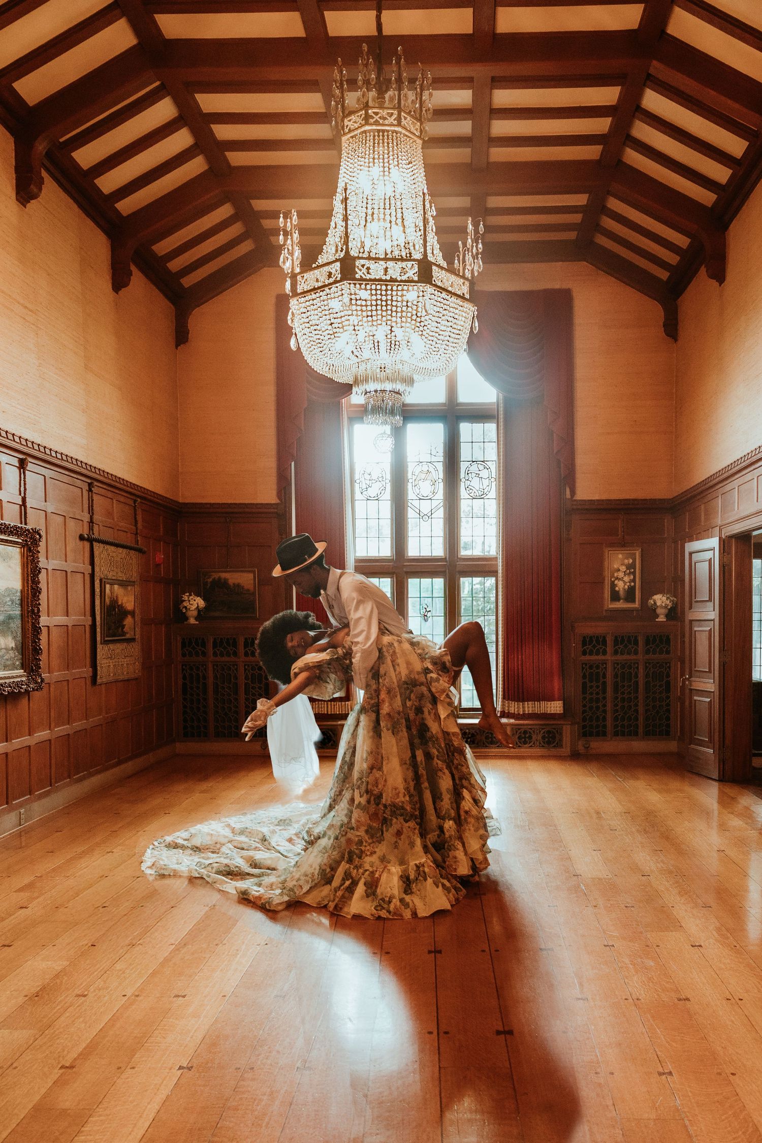 Elegant ballroom with wooden floors, crystal chandeliers, and ornate wood paneling features a dramatic tree sculpture.