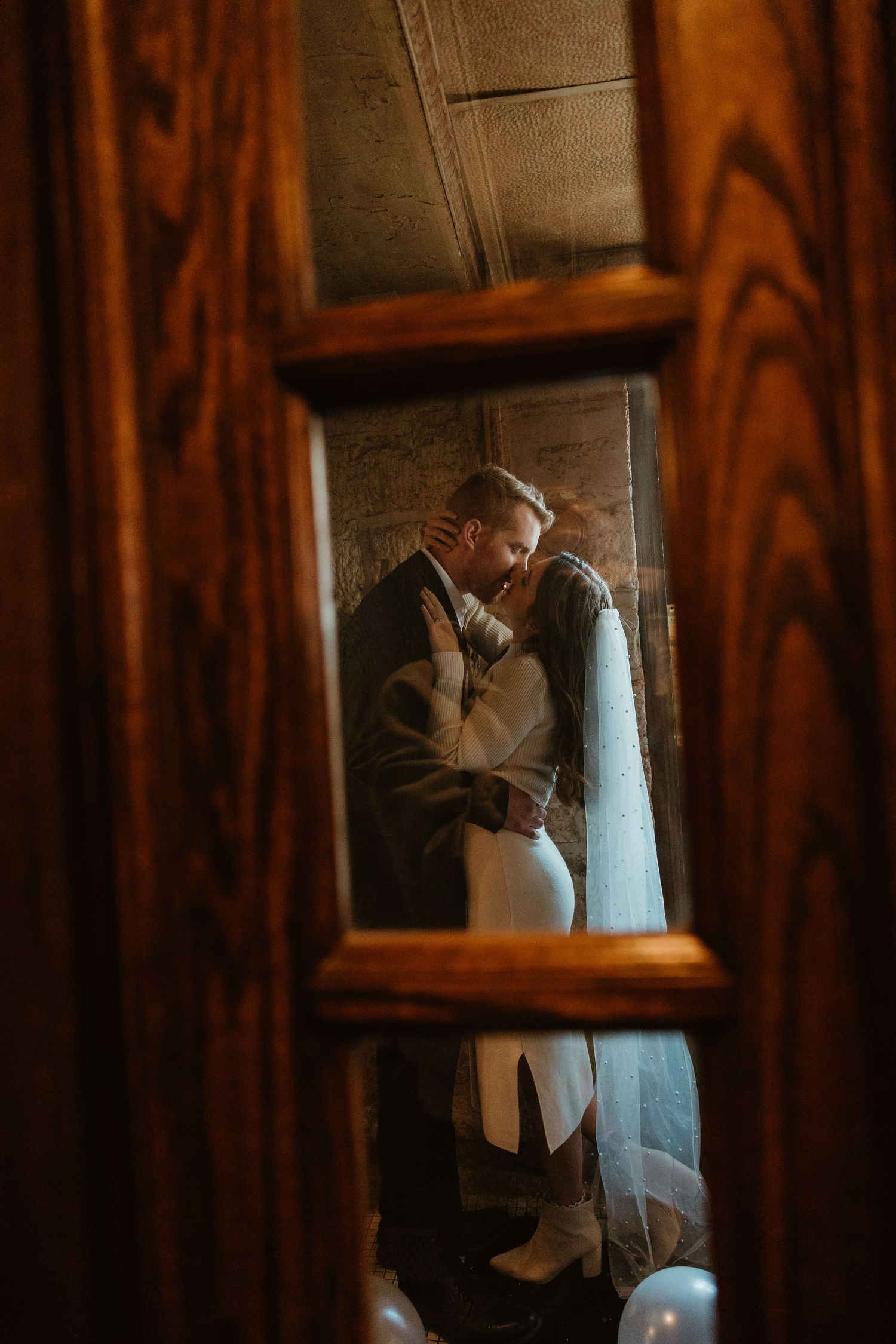 A romantic couple shares an intimate moment in a dimly lit hallway with wooden paneling.