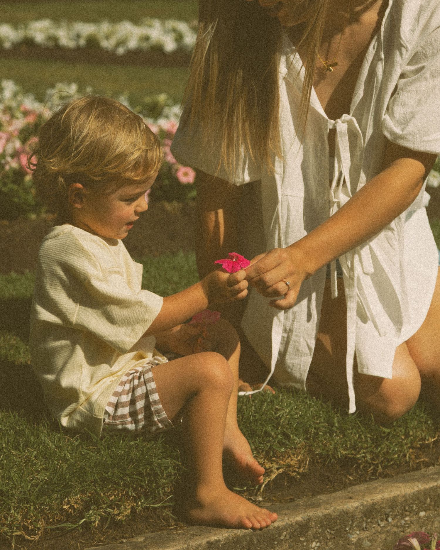 People sitting on grass with bare feet near pink flowers in vintage-tinted photography.