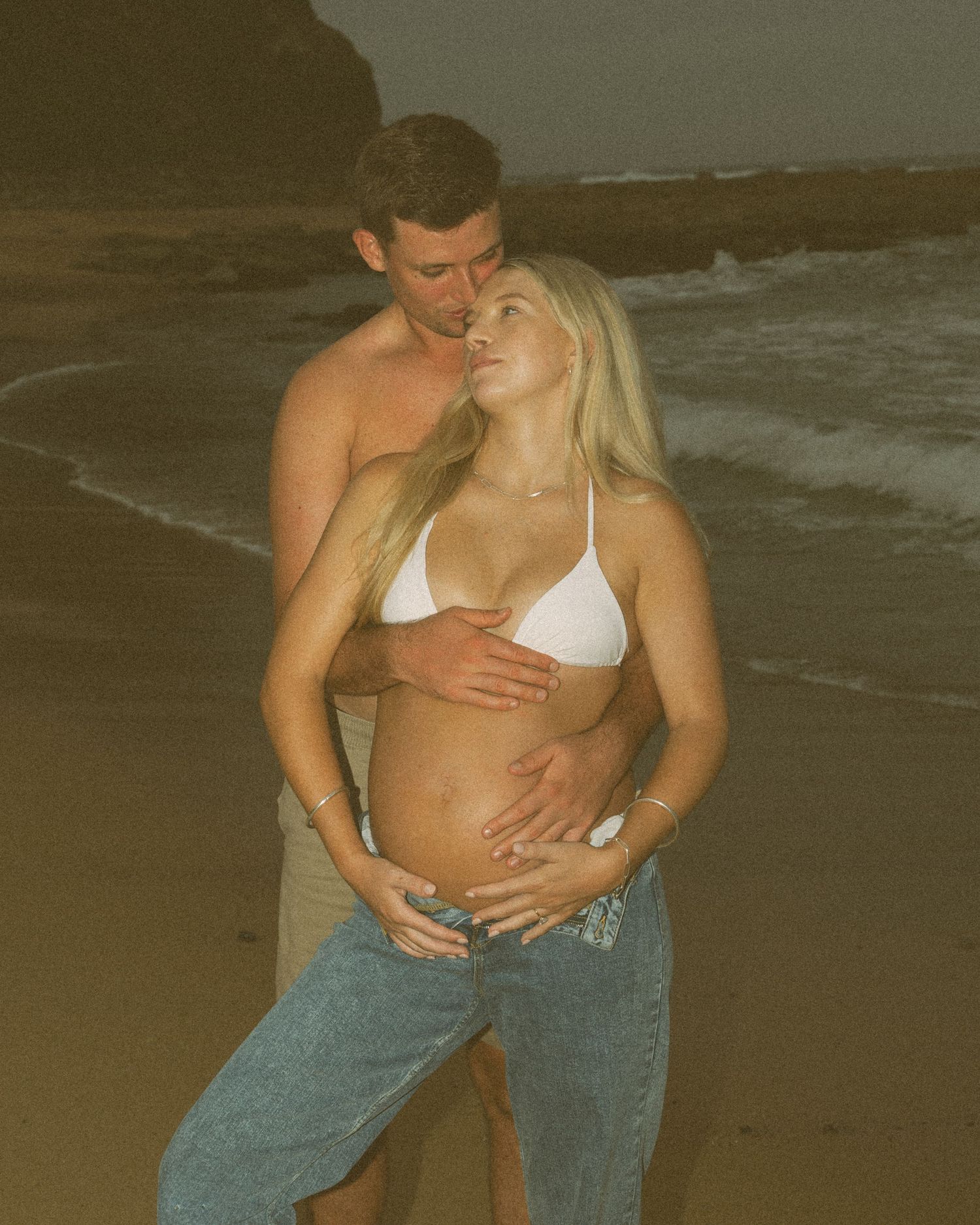 Intimate couple embracing on beach at sunset in casual attire.