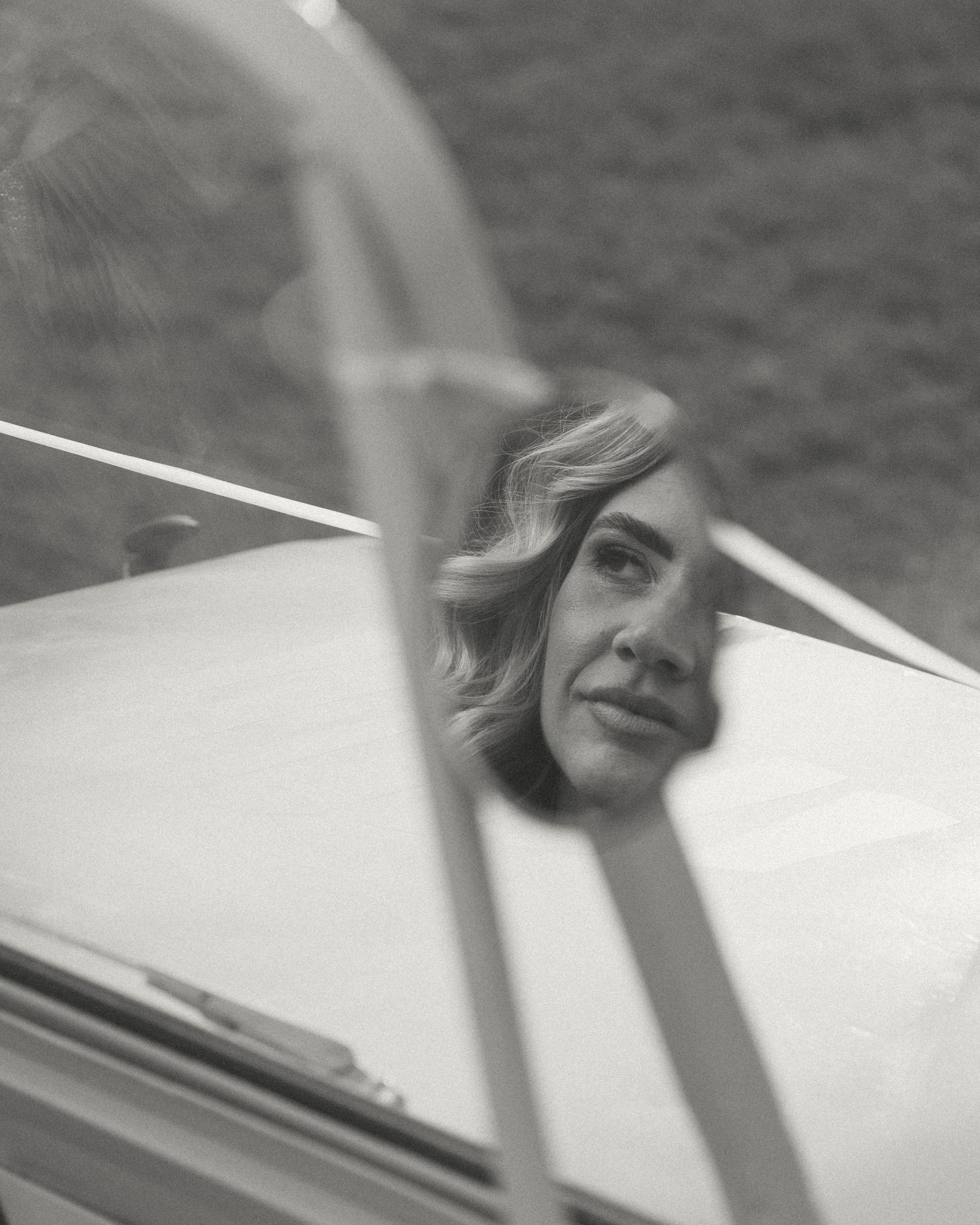 Black and white photo of a woman's reflection in a car mirror, with wavy hair and a serene expression.
