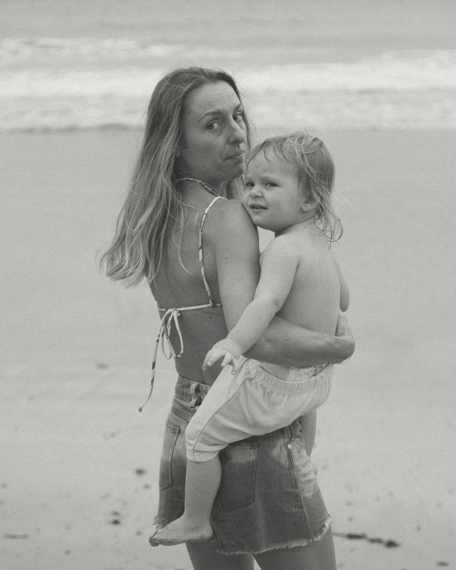 A tender moment captured in black and white as a parent and child embrace on a serene beach.