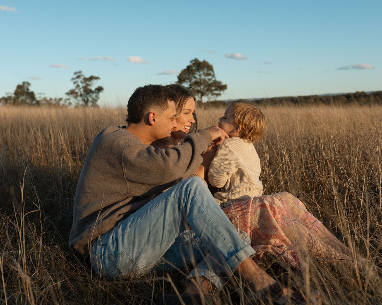 Couple relaxing together in tall grass field during golden hour sunset.
