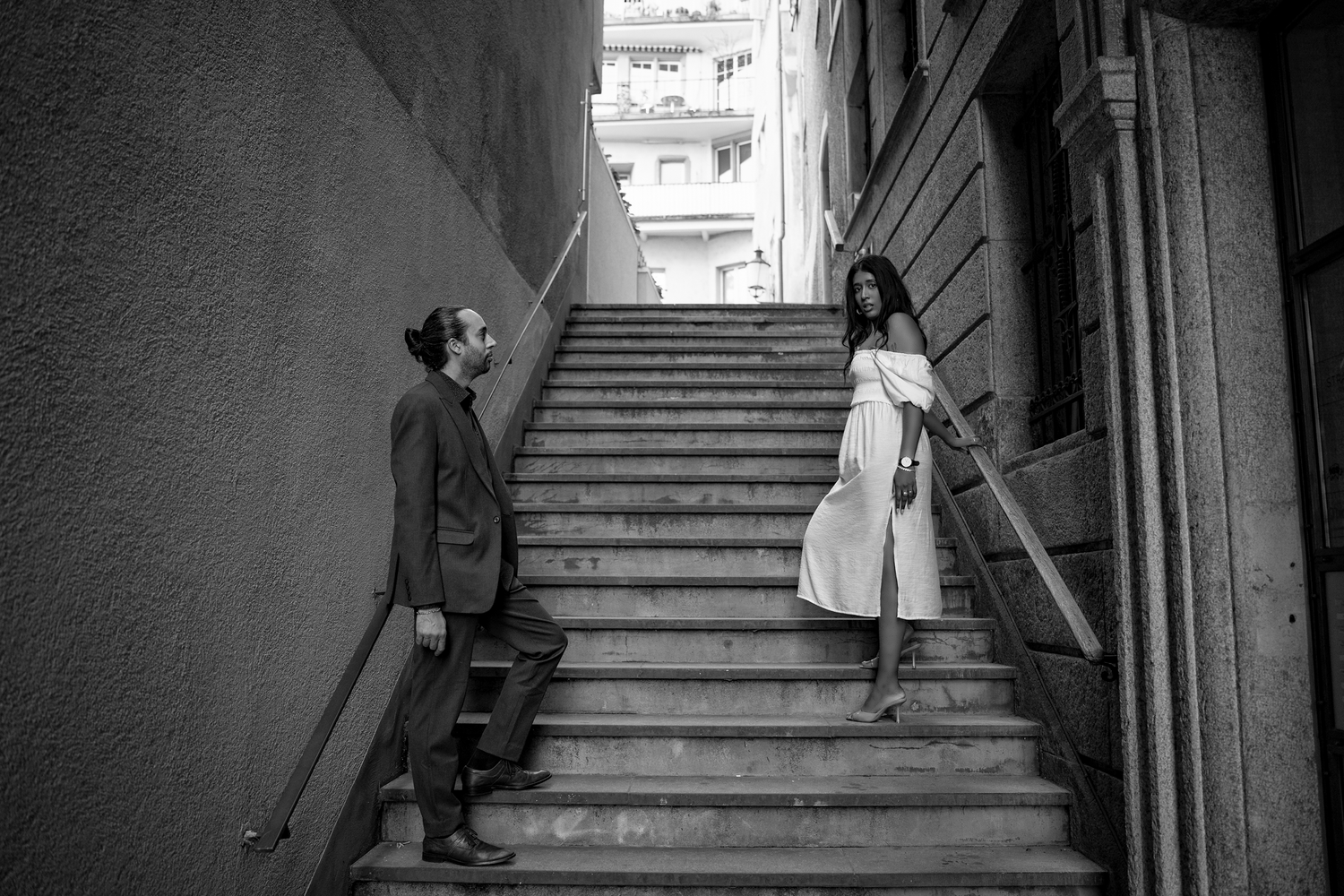 Black and white photo of a man and woman conversing on outdoor stone stairs in an urban alleyway.