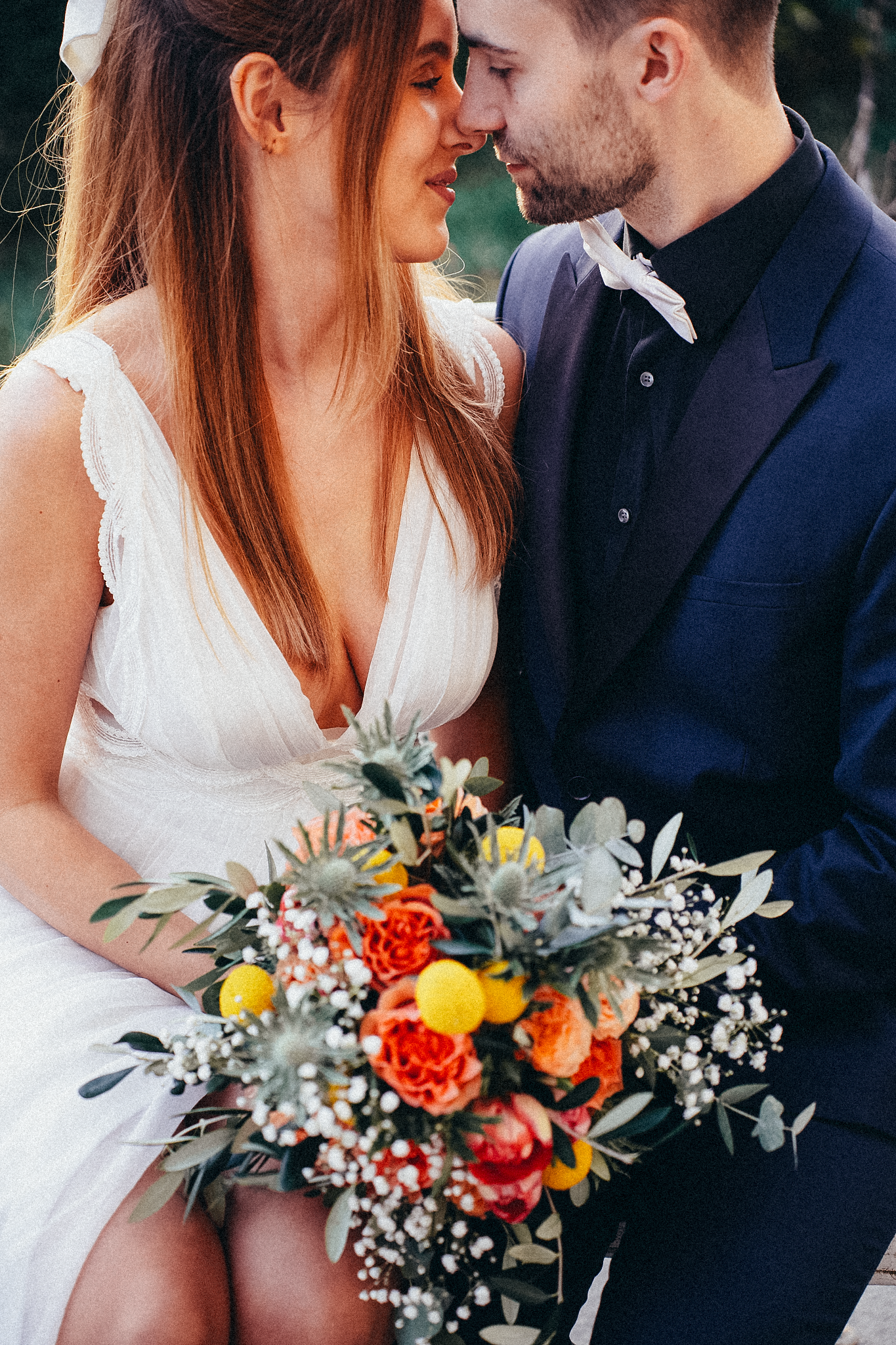 Close-up of wedding couple nearly kissing while holding lush bouquet with orange roses and eucalyptus.