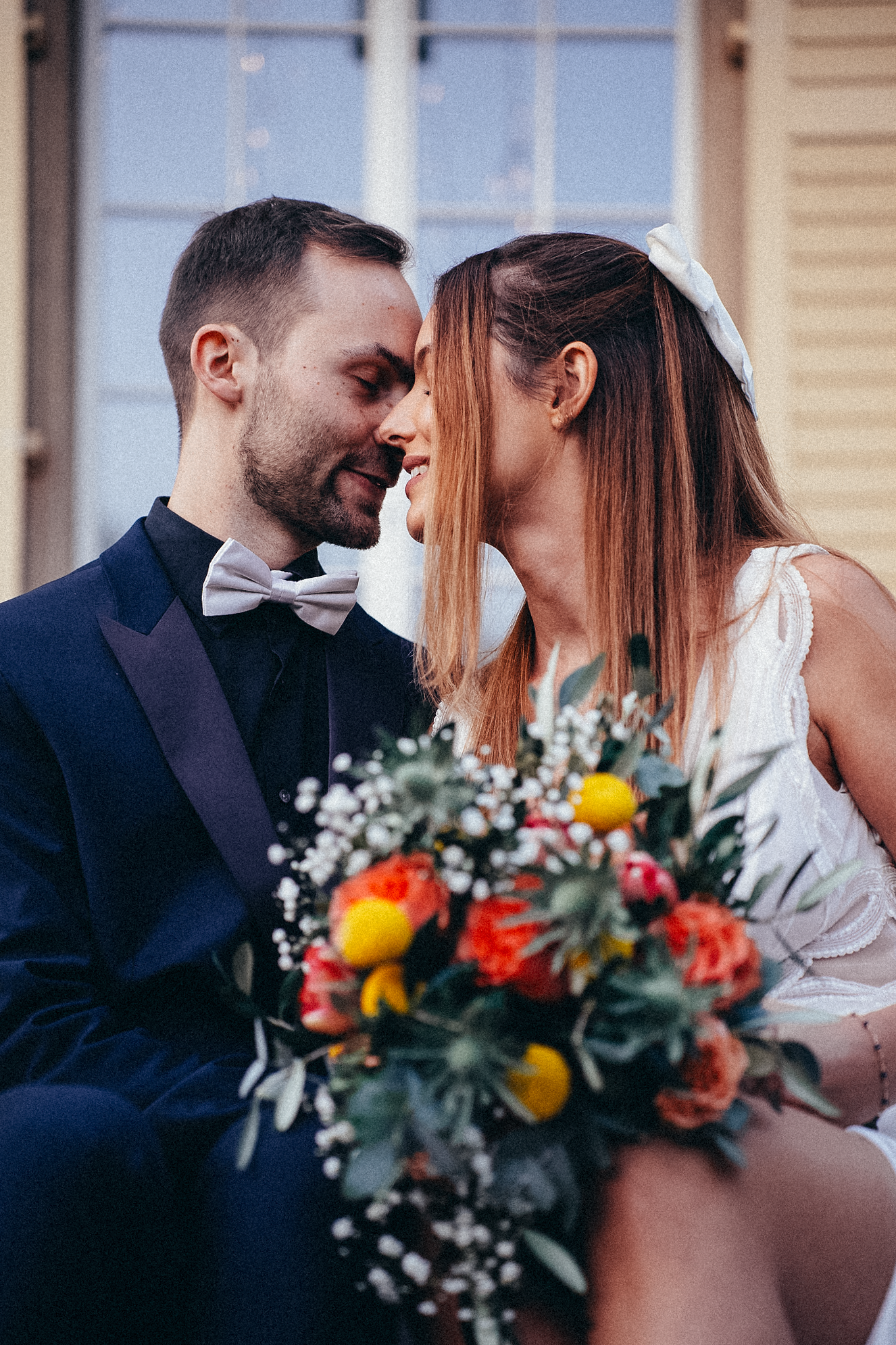 Bride and groom sharing an intimate nose-to-nose moment with colorful floral bouquet in the foreground.