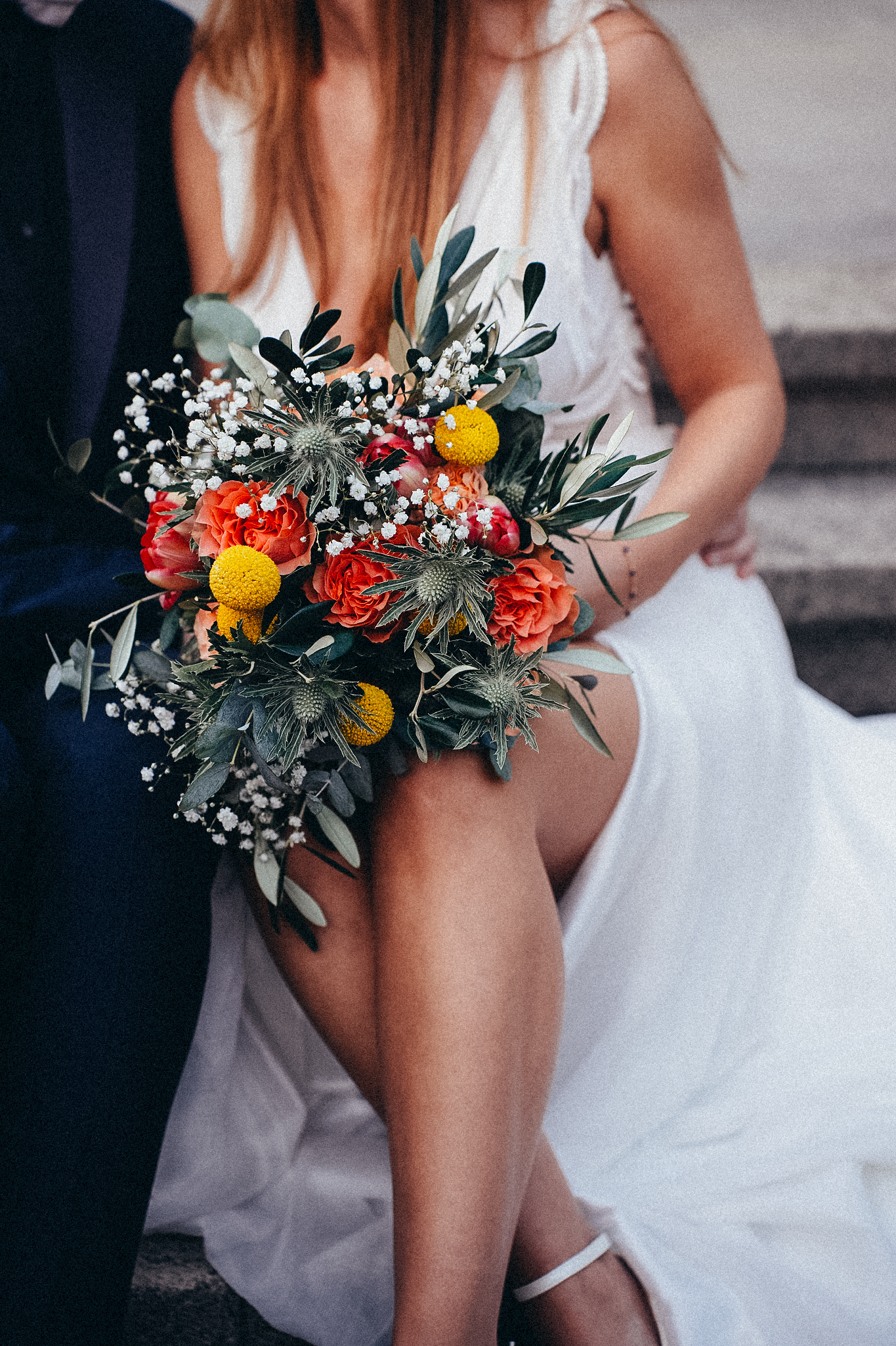 Close-up of bridal bouquet with orange roses, yellow billy balls, white gypsophila, and eucalyptus greenery.