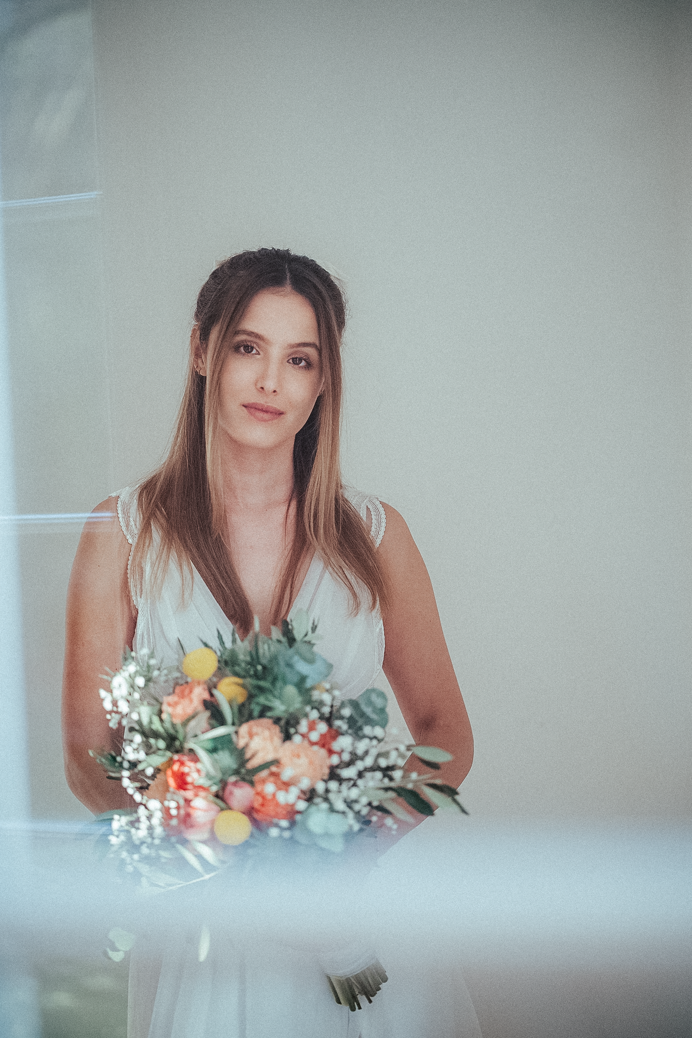 A bride in a white dress holds a colorful bouquet of flowers while posing indoors.