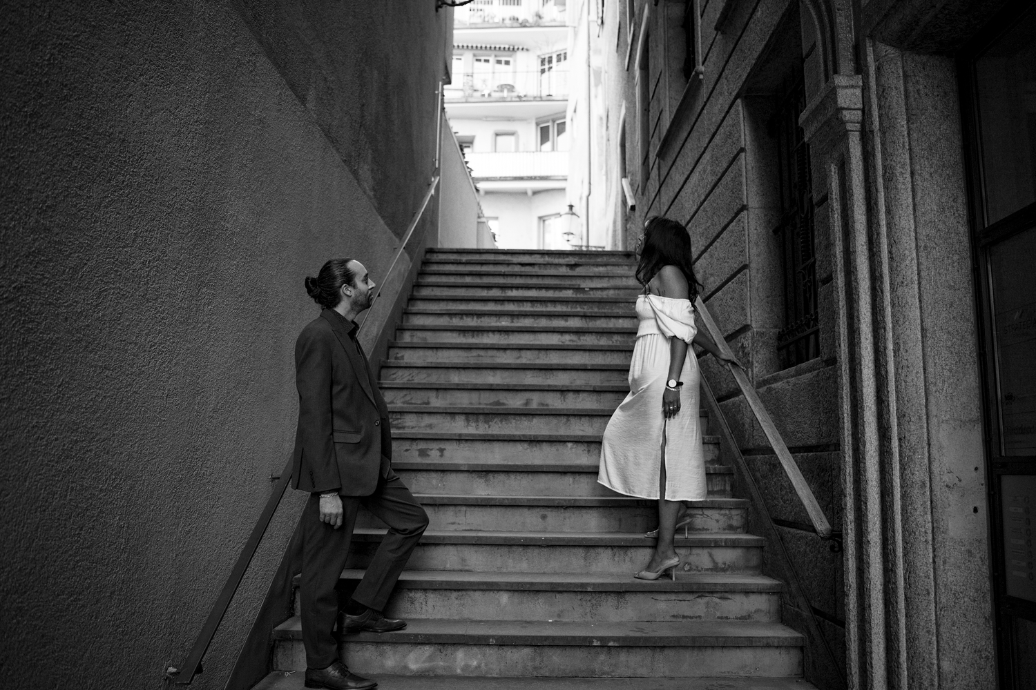 Black and white photo of a man in a suit and a woman in a dress on a narrow staircase, conveying a contemplative mood.