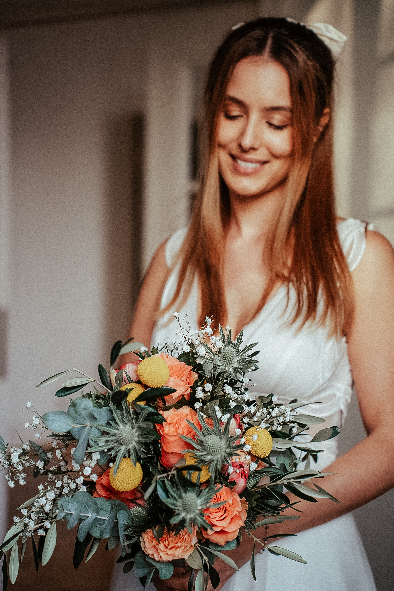 Smiling bride in white dress holding a colorful bouquet of orange roses, yellow flowers, and eucalyptus greenery.