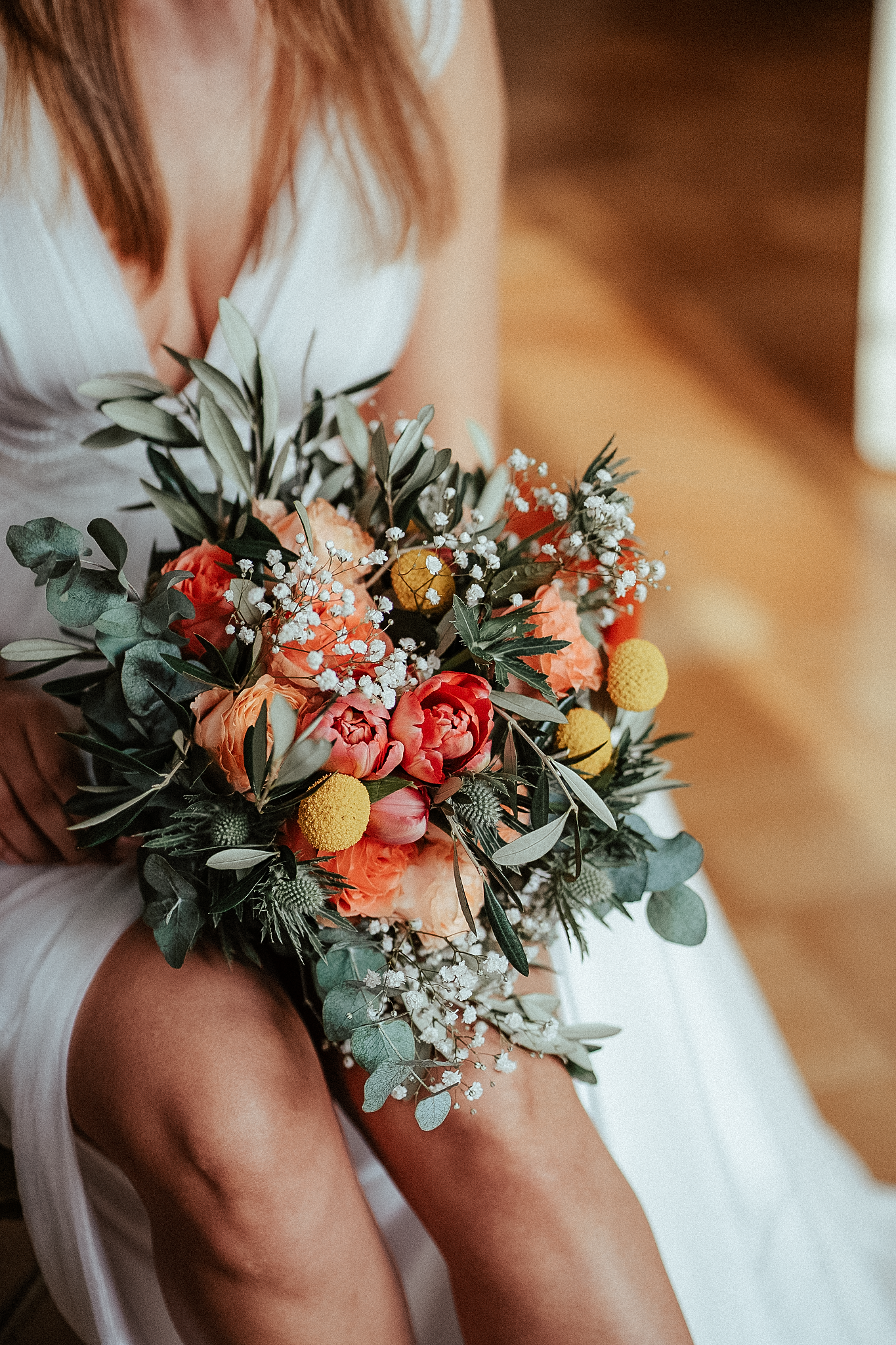 Bride in white dress holding a vibrant wedding bouquet with orange peonies, yellow billy balls, eucalyptus, and baby's breath.