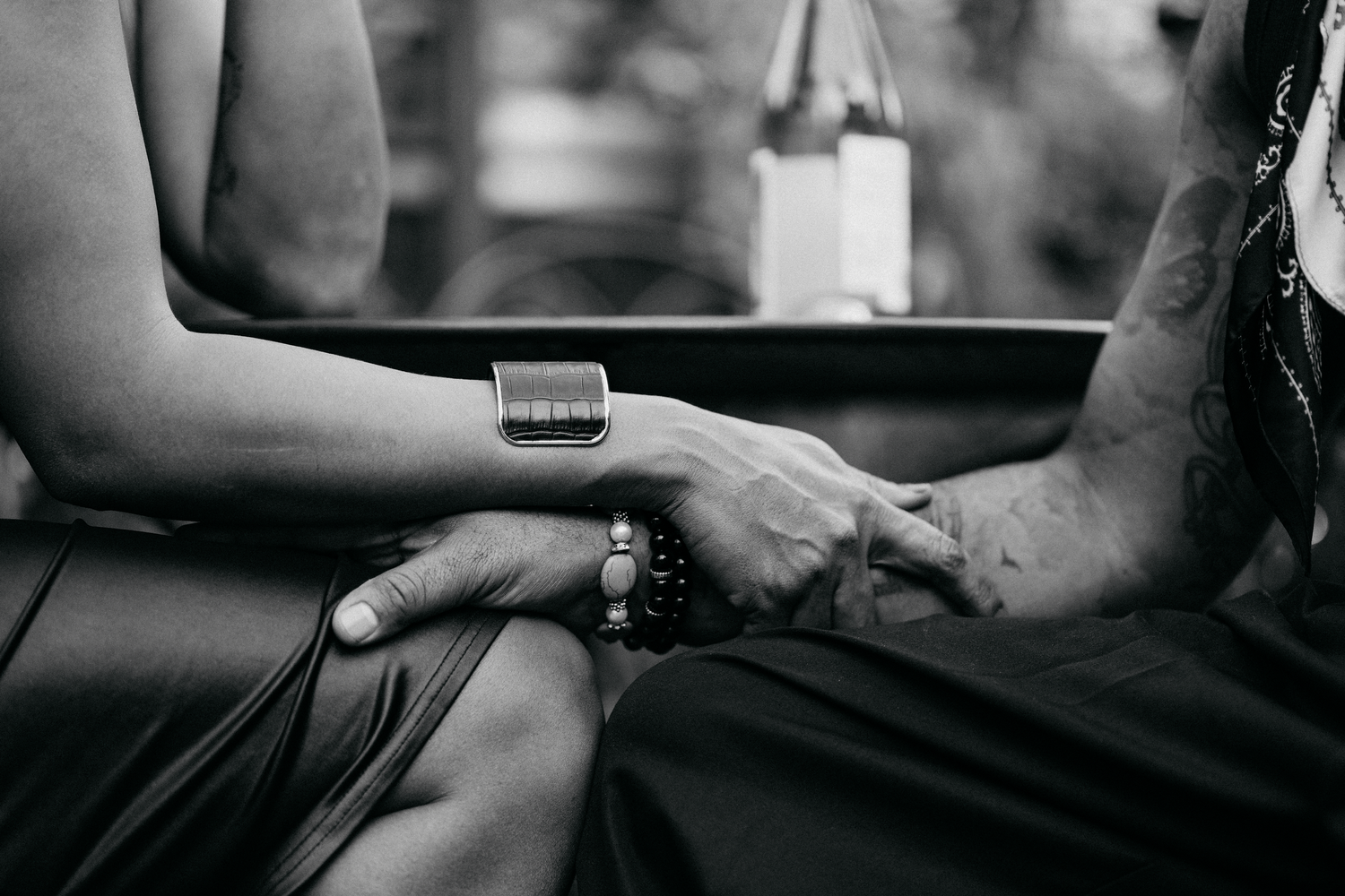 Black and white close-up of two people holding hands, one wearing a smartwatch and beaded bracelet.