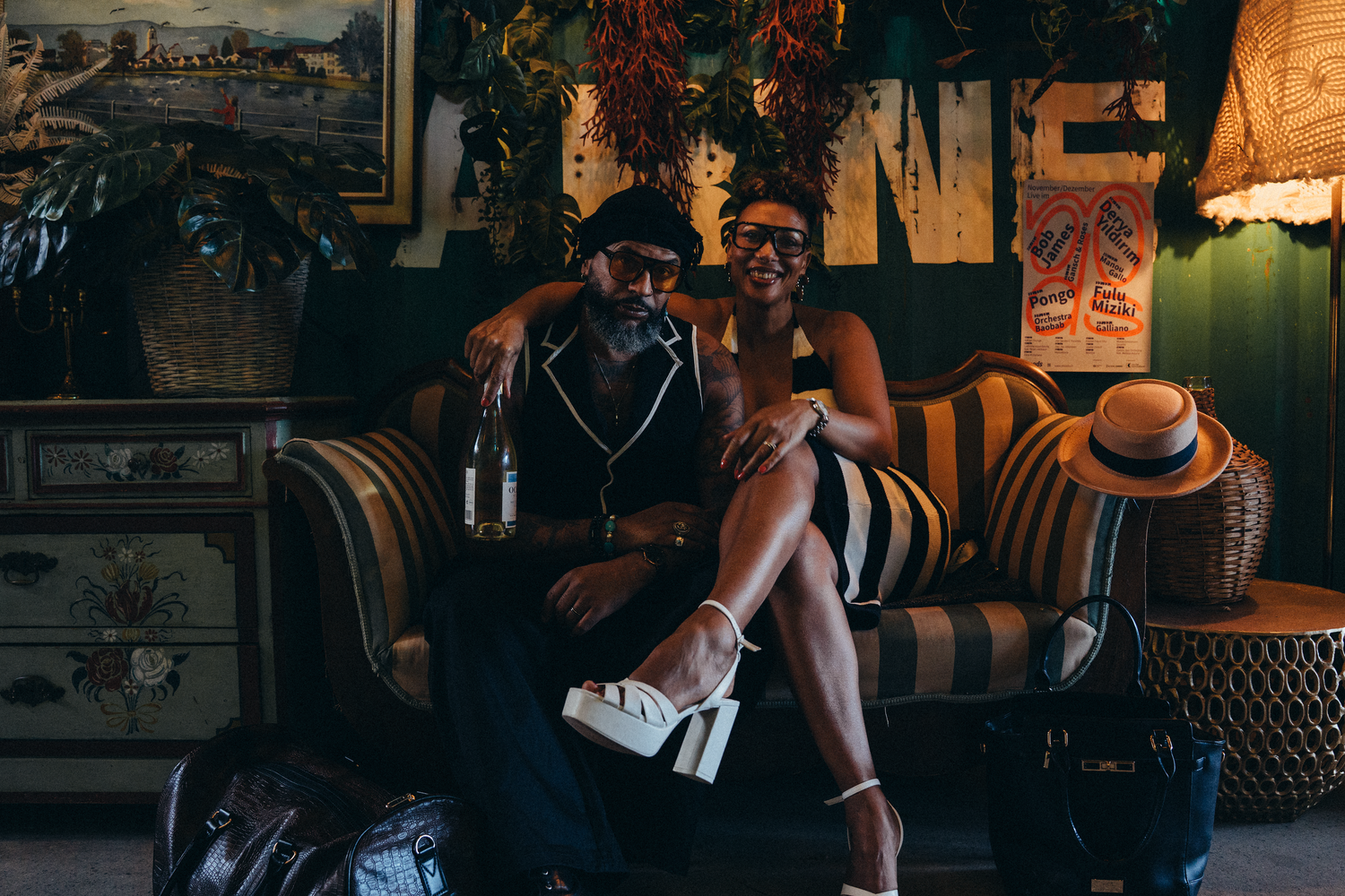Couple posing together on a vintage striped sofa in a bohemian decorated interior with tropical decor.