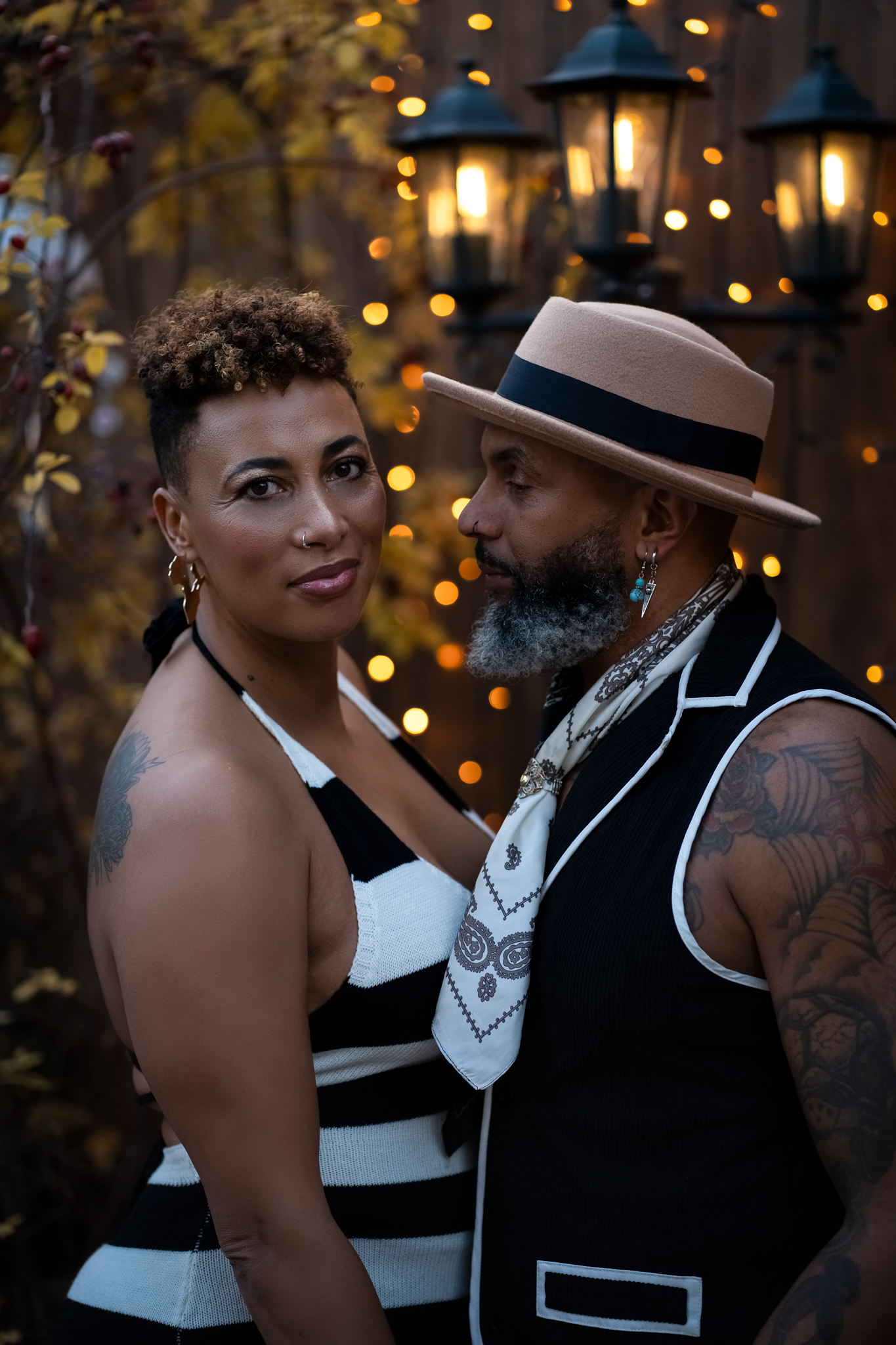 A couple stands closely, gazing at each other with gentle expressions. They are surrounded by warm, glowing fairy lights and vintage lamps