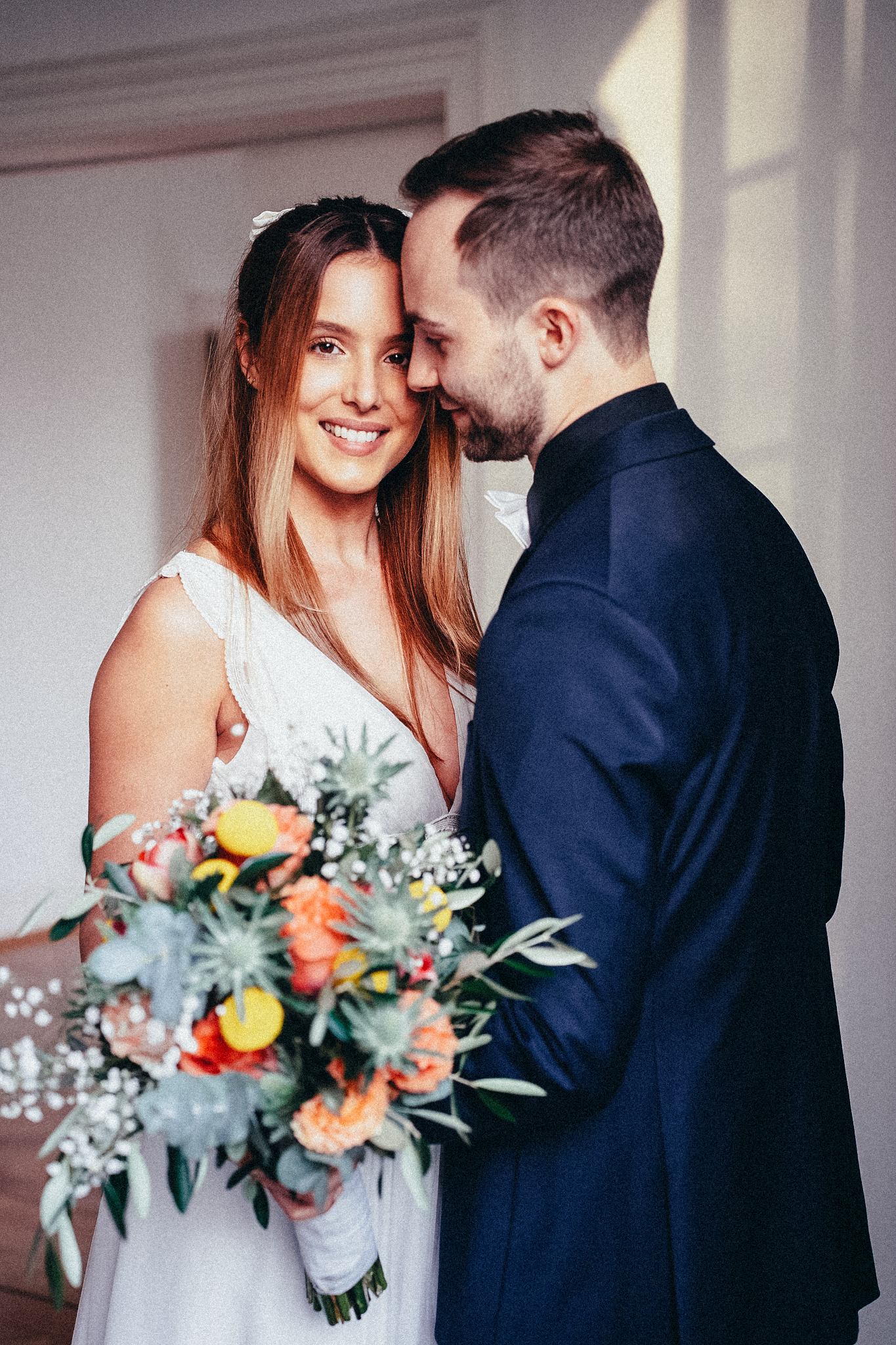 Romantic wedding couple sharing an intimate moment, bride in white gown holding colorful floral bouquet.