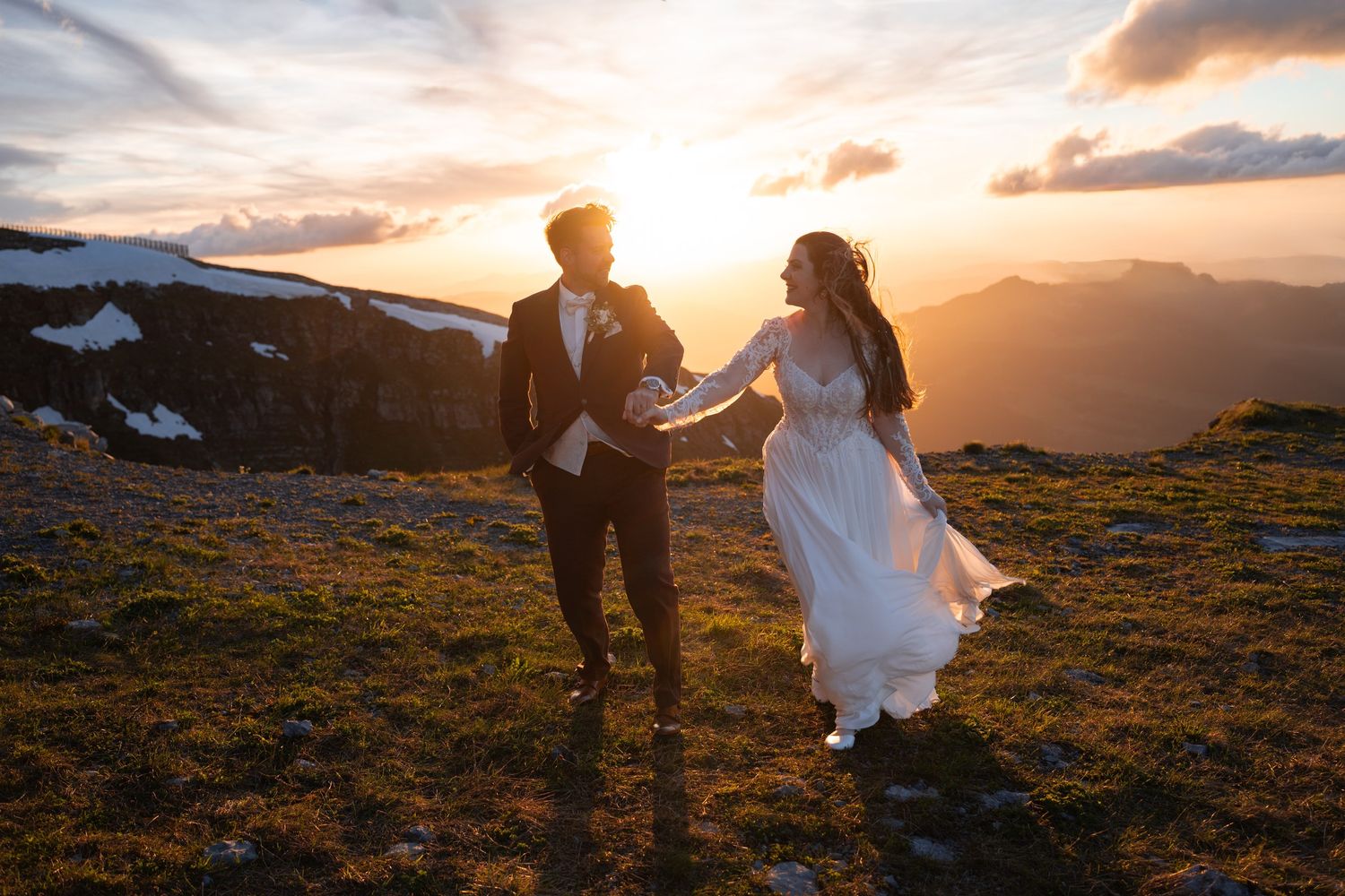 Bride and groom hold hands running on mountain summit at golden sunset during outdoor elopement wedding ceremony.