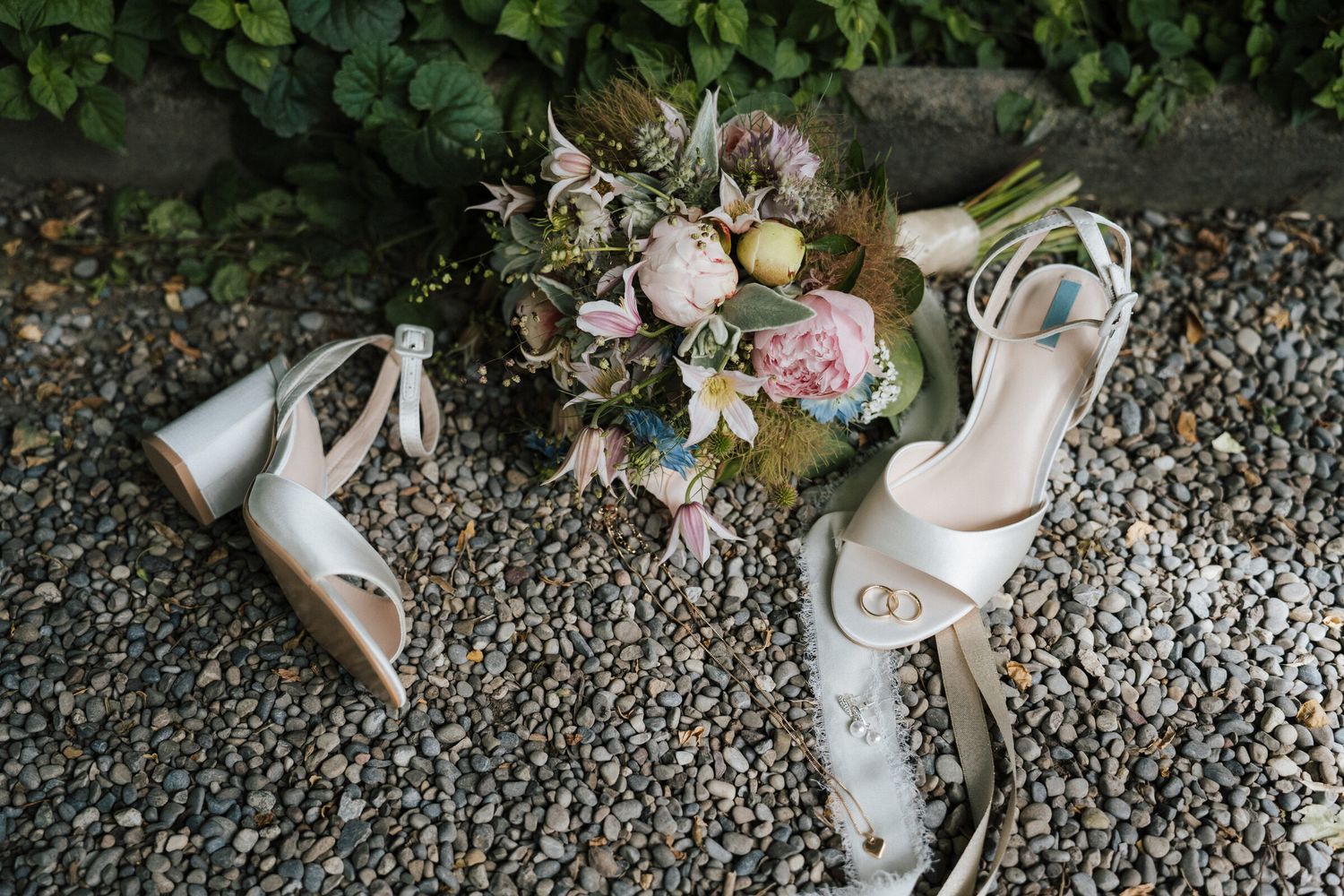 Bridal heels and floral bouquet with pink peonies arranged on stone gravel, perfect for a romantic wedding day.