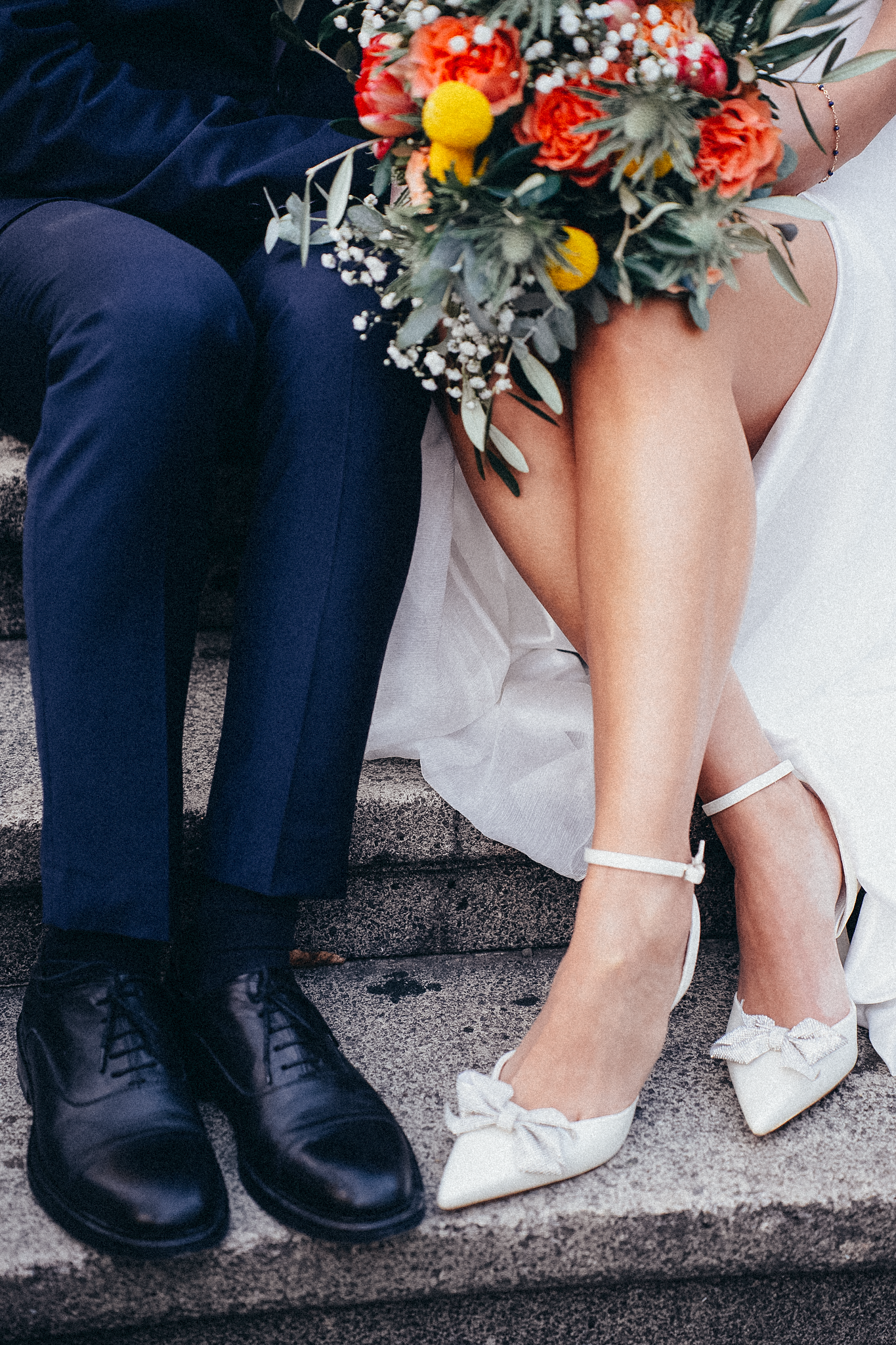 Close-up of wedding couple's feet on steps, bride wearing white bow heels, groom in black Oxford shoes.