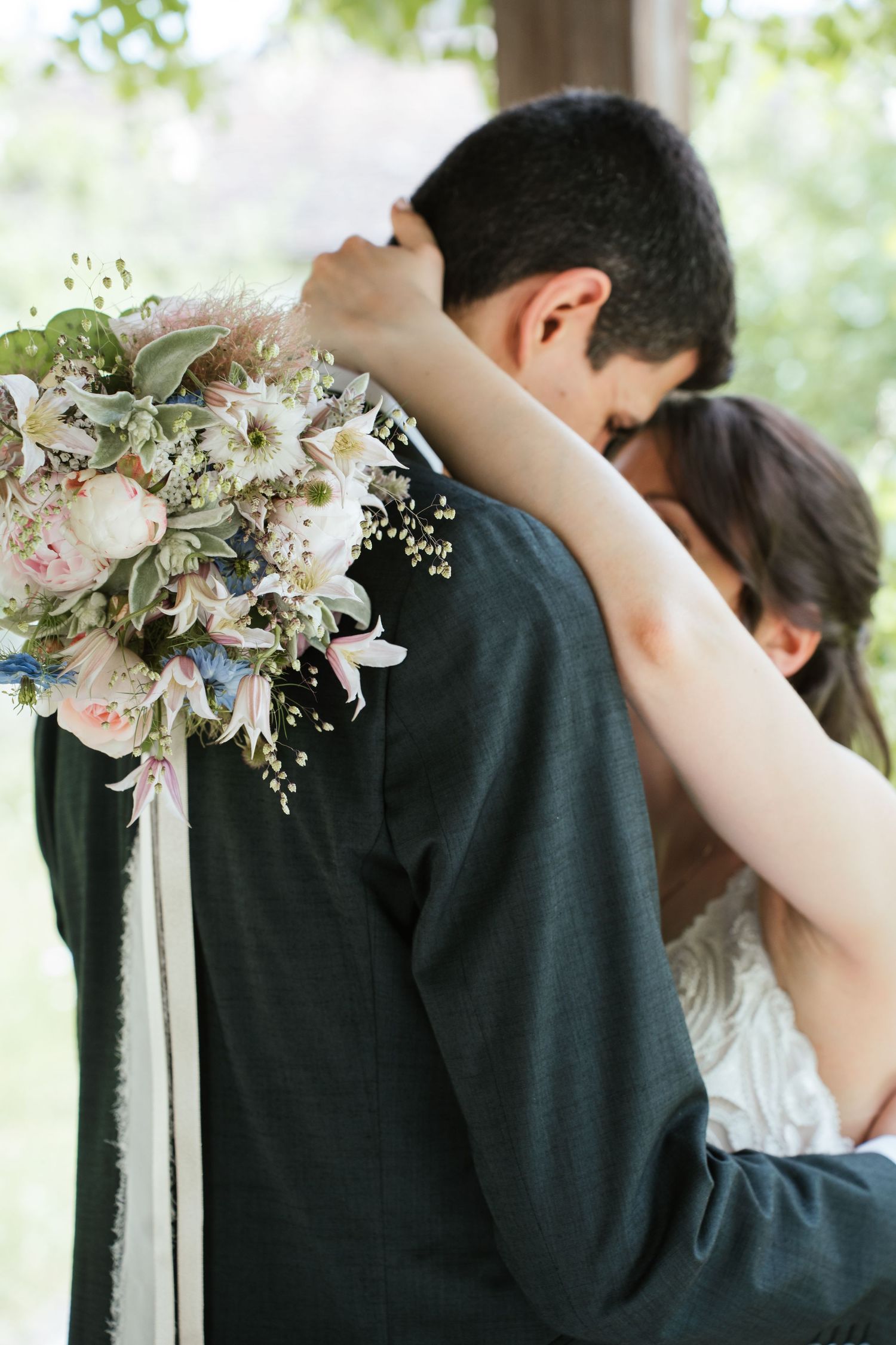 Bride and groom embracing tenderly, bride holding a soft pastel wedding bouquet with peonies and wildflowers.