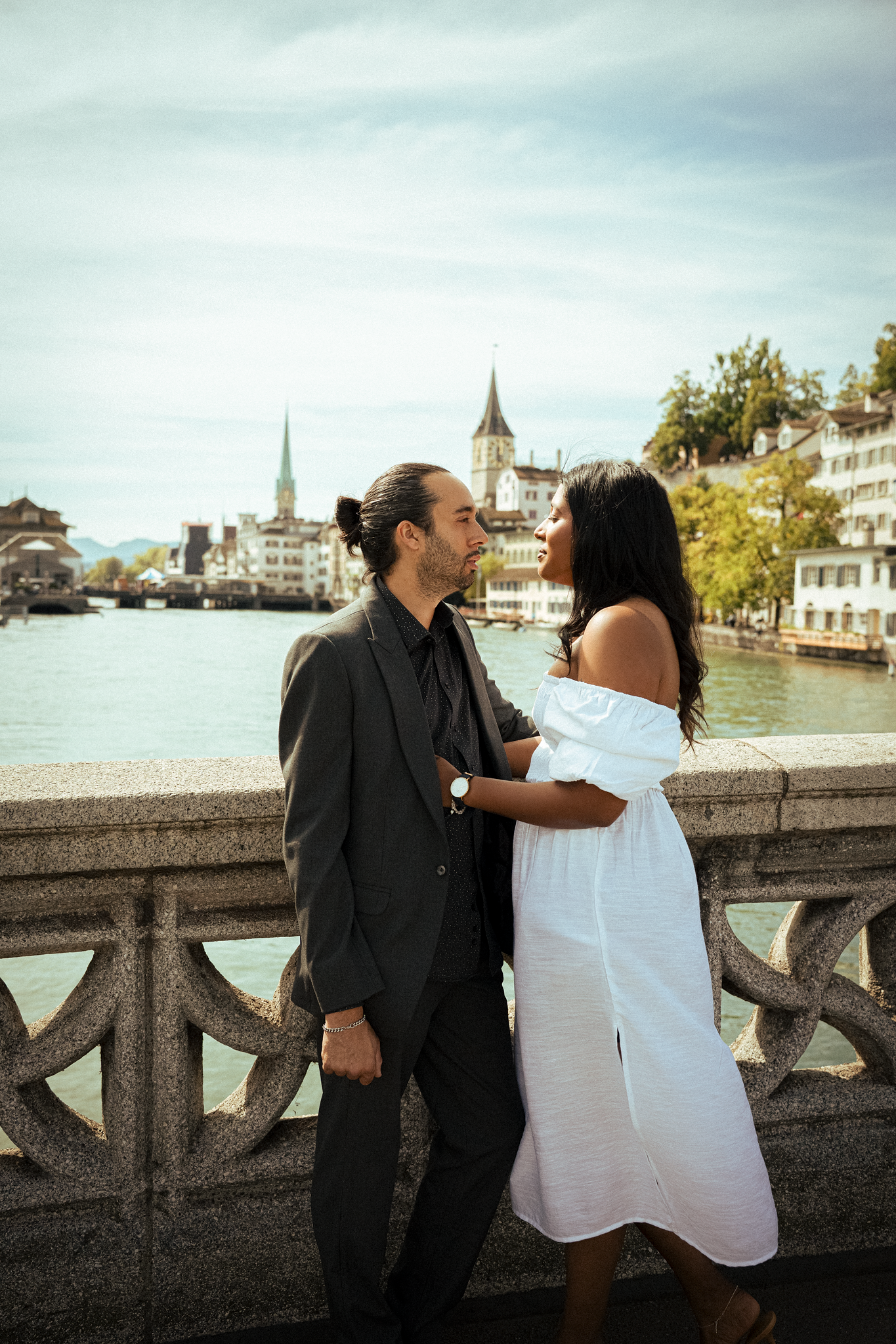 Couple in elegant attire sharing a romantic moment on a bridge overlooking Zurich river and historic skyline.