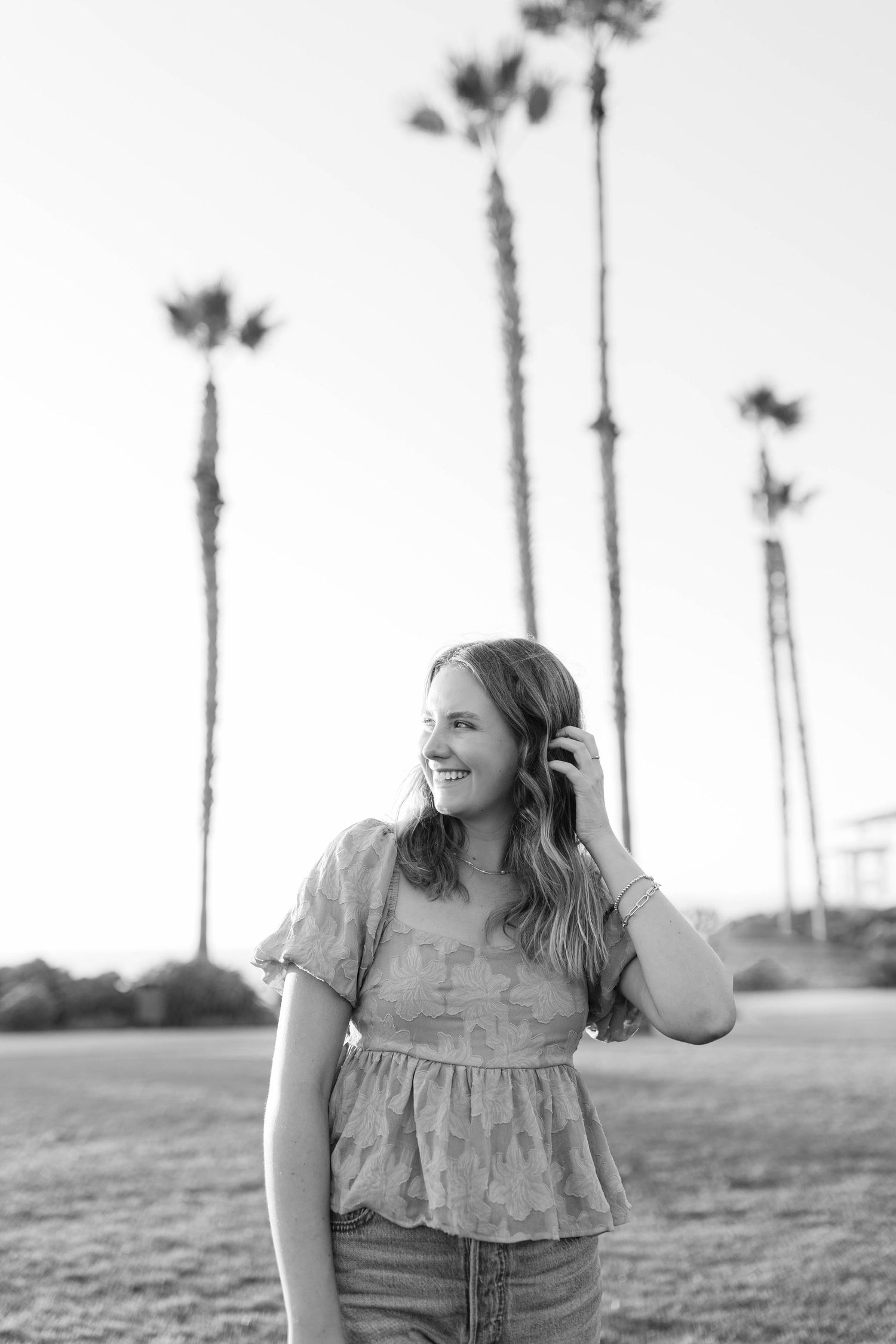 A black and white photo series of someone in a floral top and jeans sitting outdoors with tall palm trees in the background.