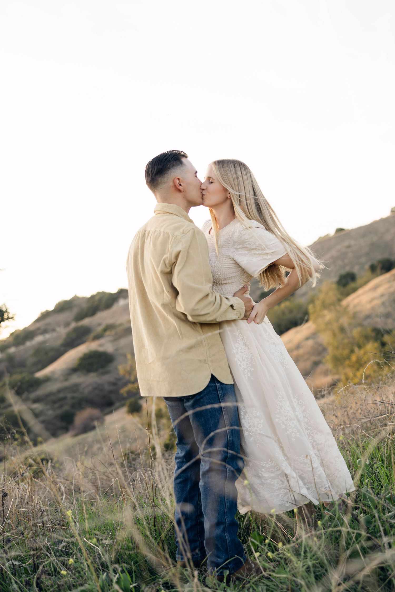 A romantic moment shared between two people on a hillside at sunset.