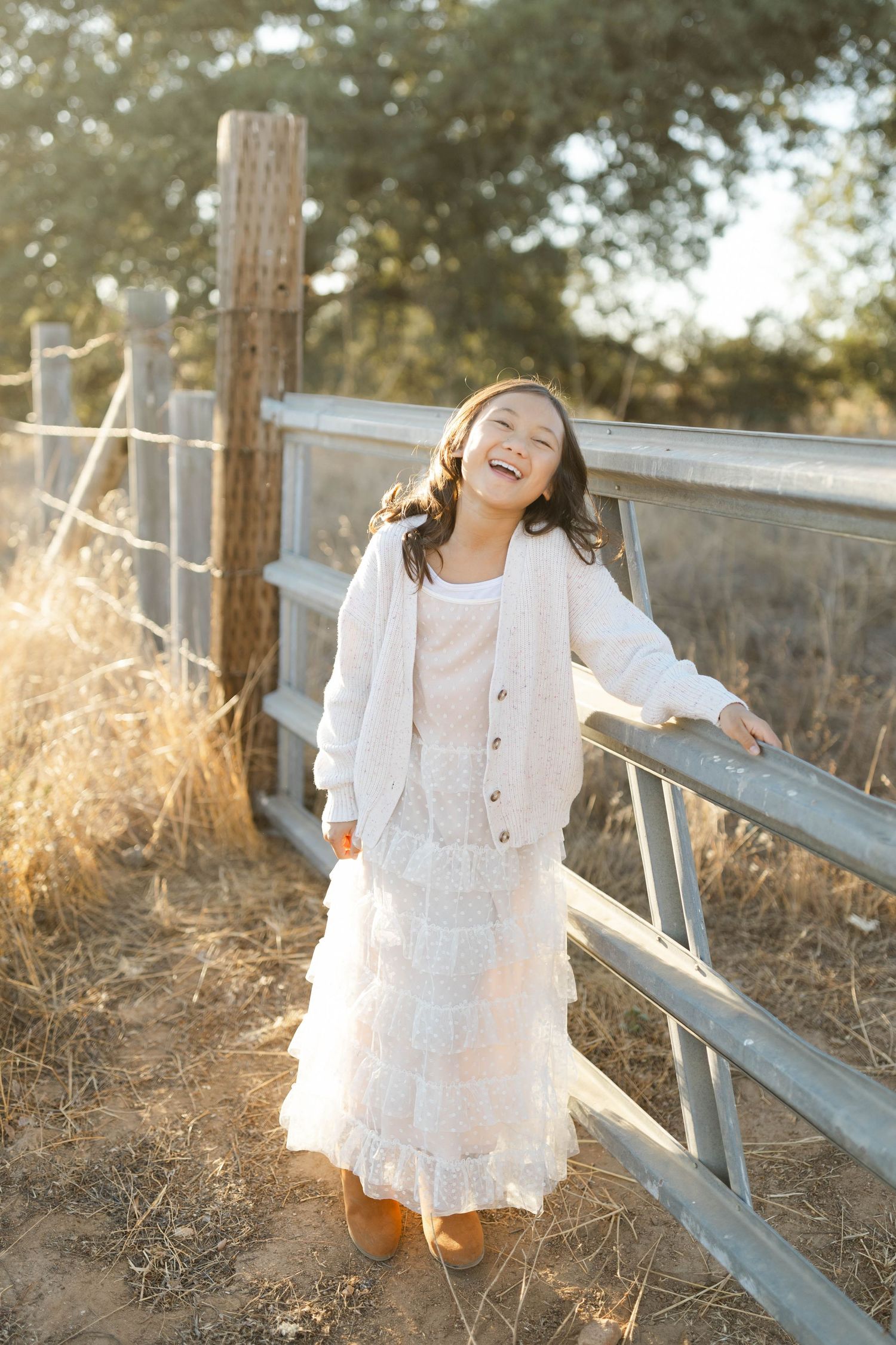 Young girl in white dress playing along a rustic fence during golden hour.