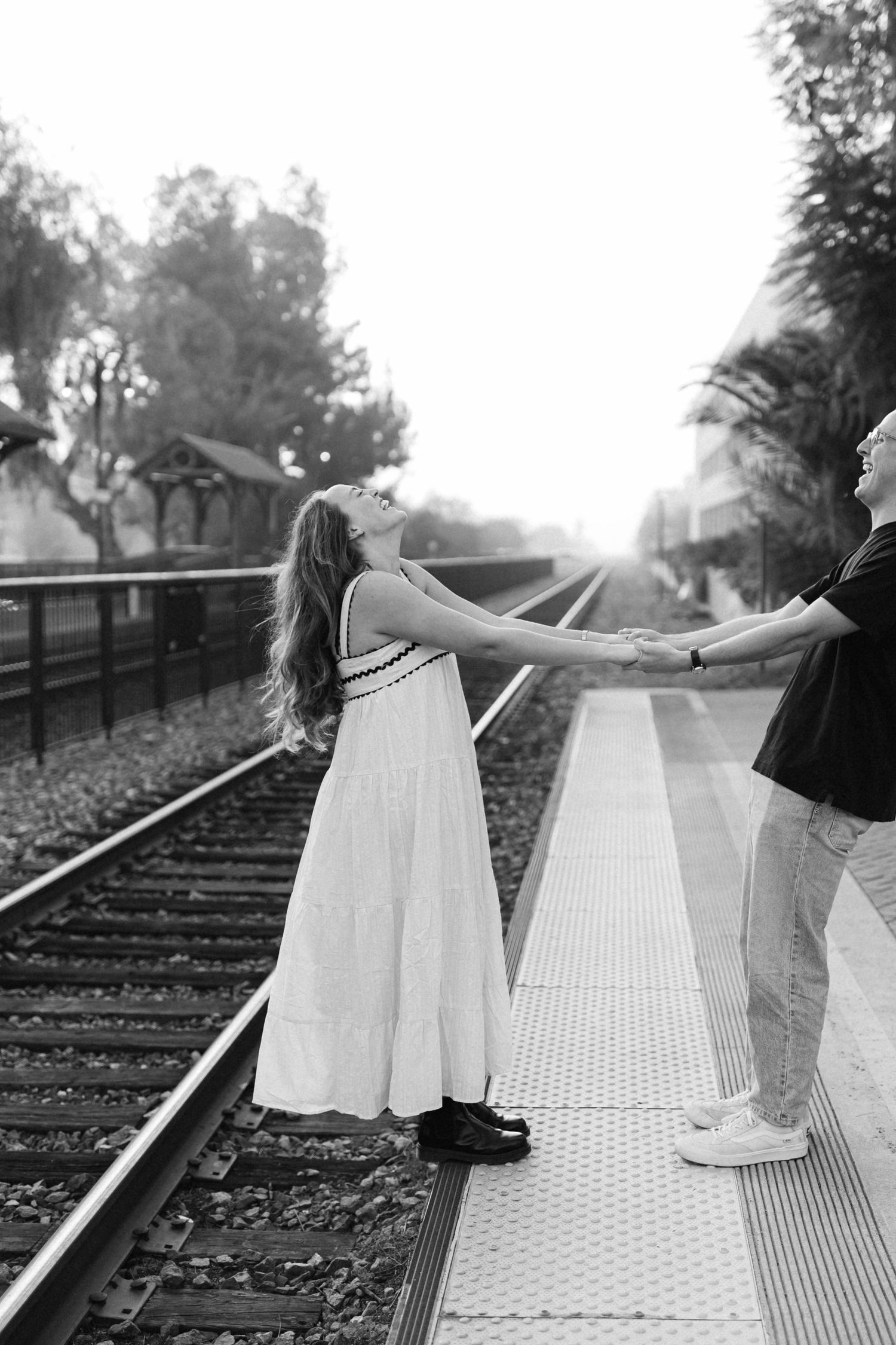 Black and white engagement photos on train tracks with couple in flowing white dress.