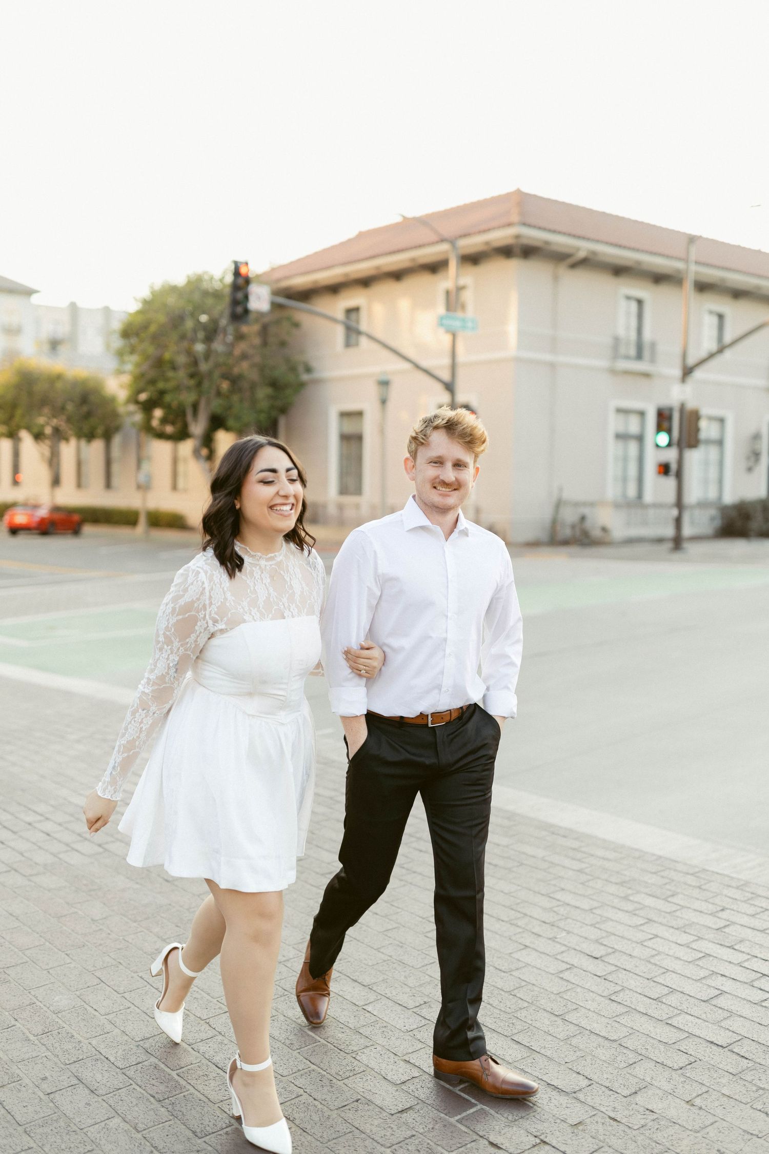 Playful couple in white and black outfits dancing and laughing together on a paved outdoor area.