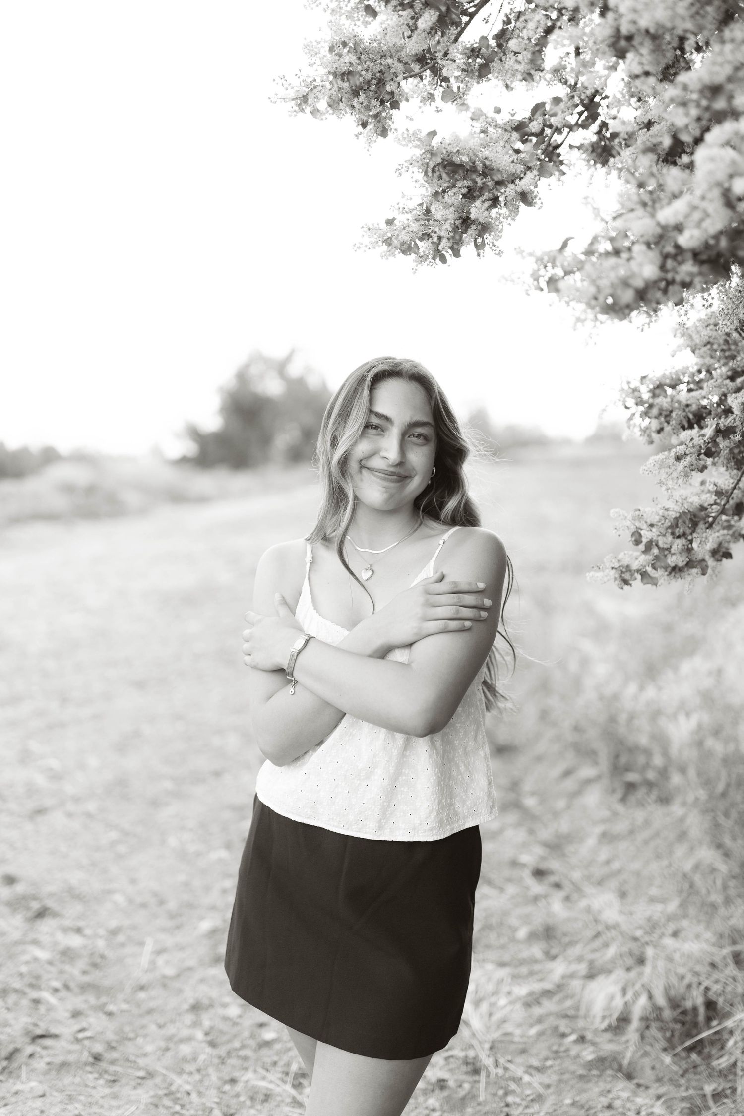 A black and white portrait of a woman in a white top and dark skirt standing outdoors.