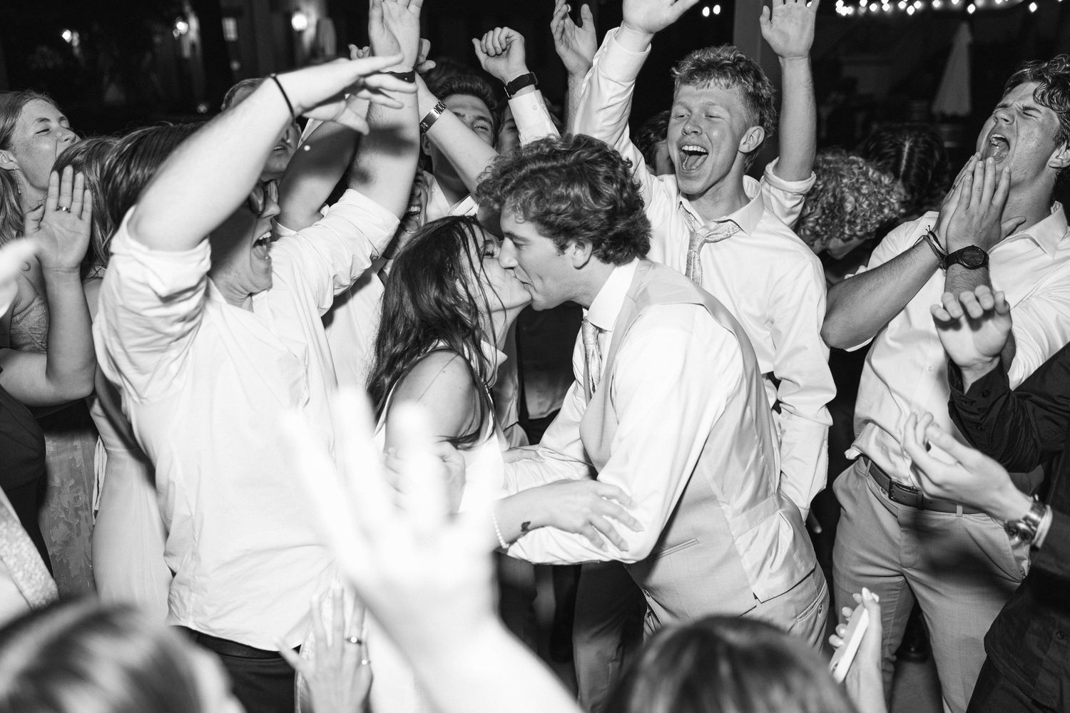 Black and white photo of wedding guests dancing and celebrating at reception.