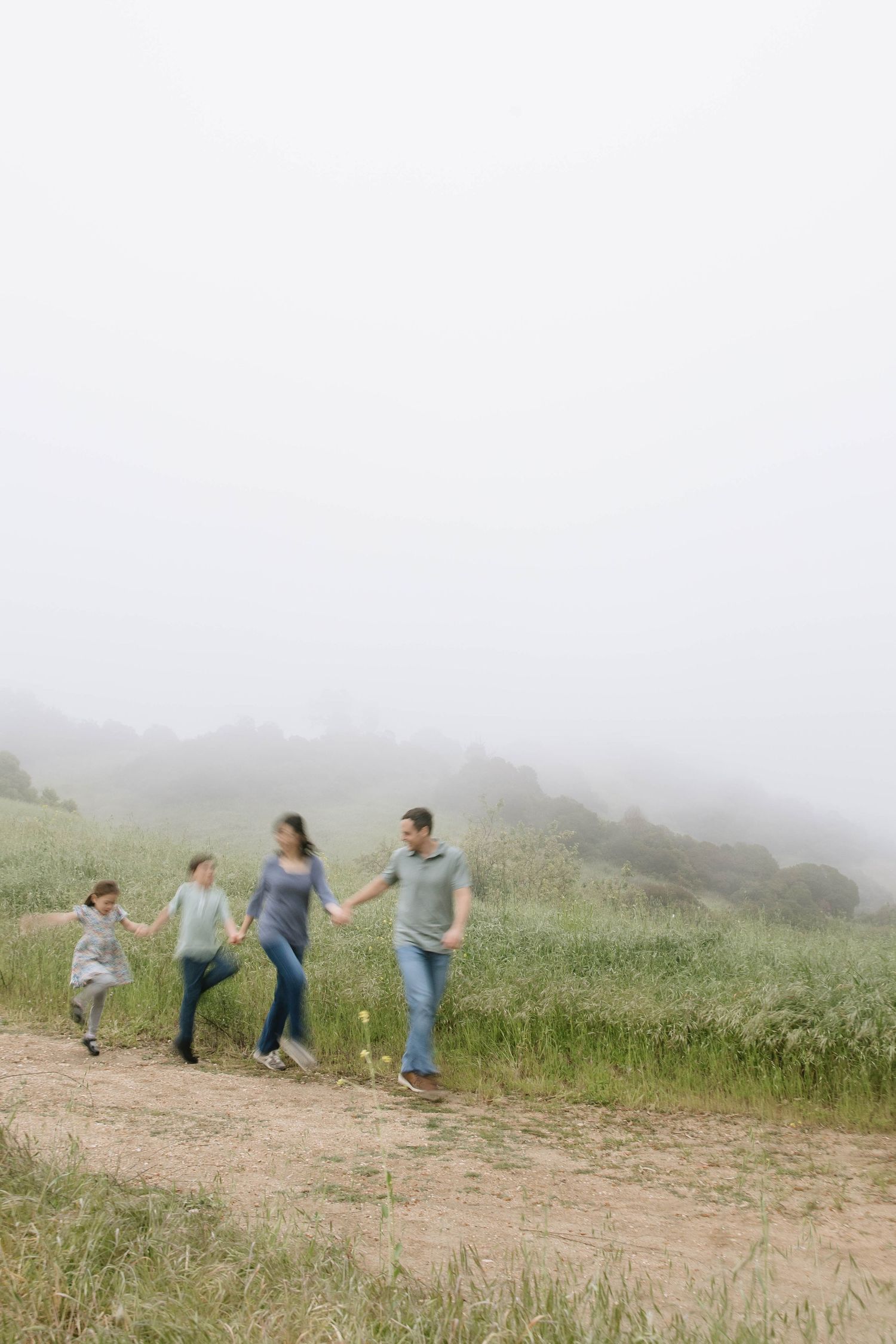 Family playing and running together in a misty field on a cloudy day.