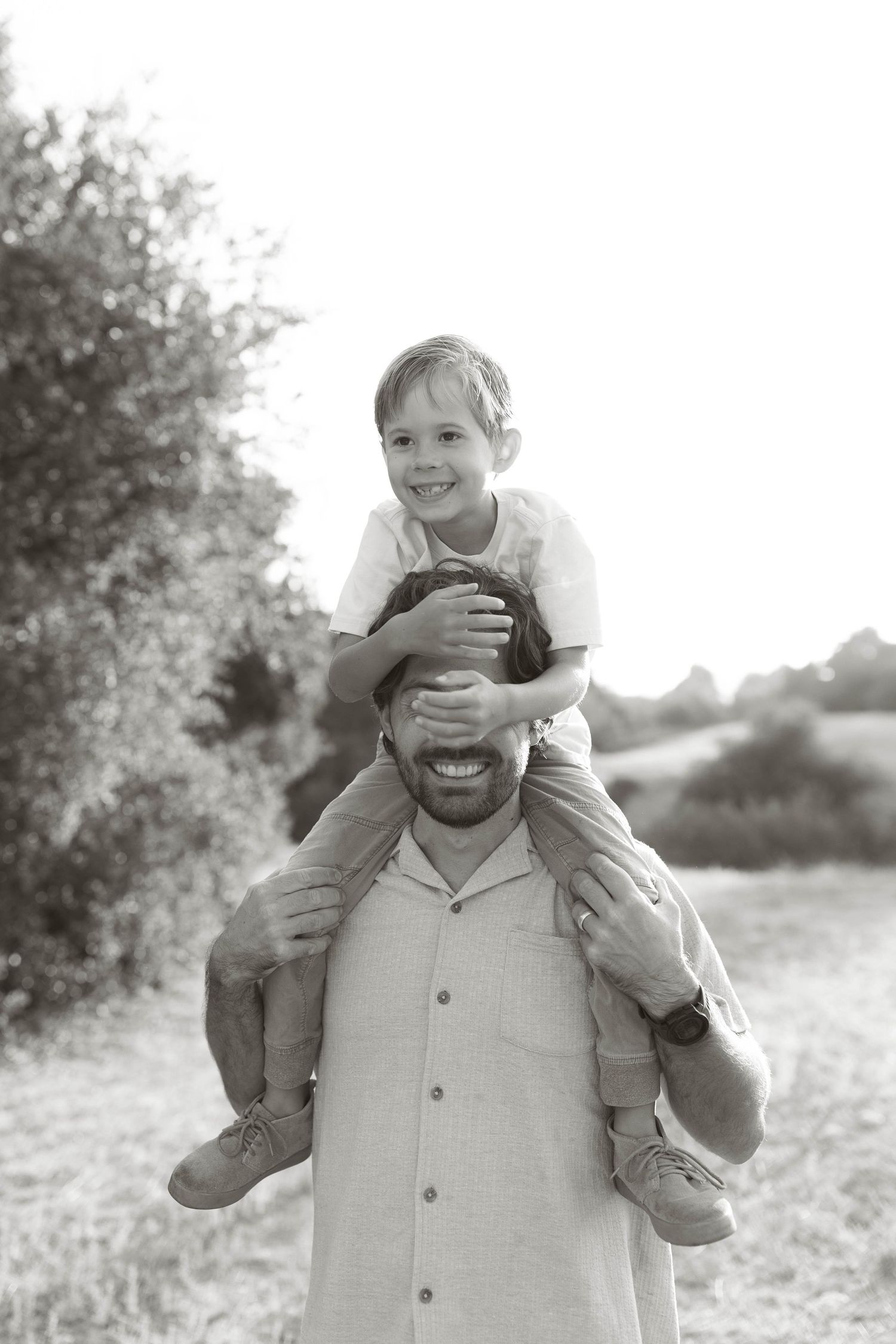 Playful moments captured between parent and child in black and white outdoor portrait.