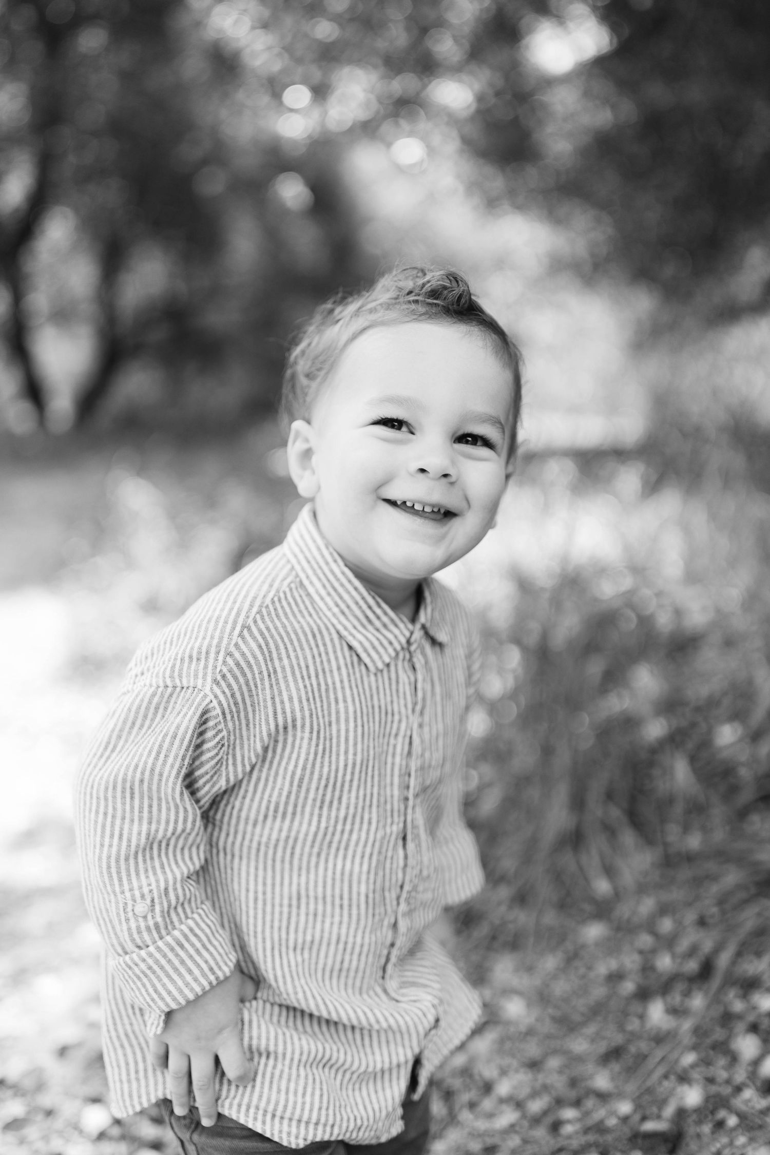 A young child in striped shirt smiles brightly in black and white portrait series.