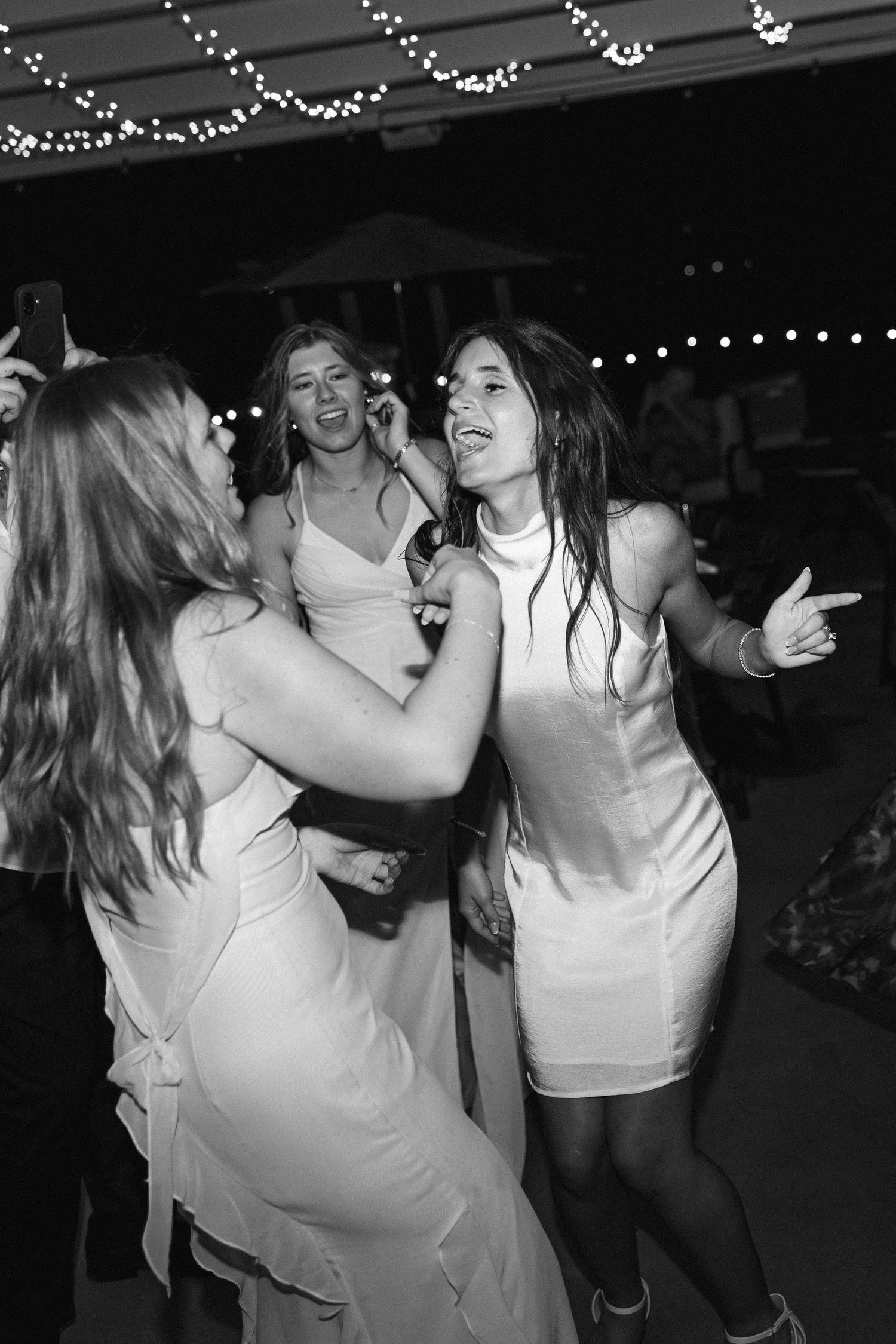 Friends dancing and celebrating joyfully at a party with string lights in the background.