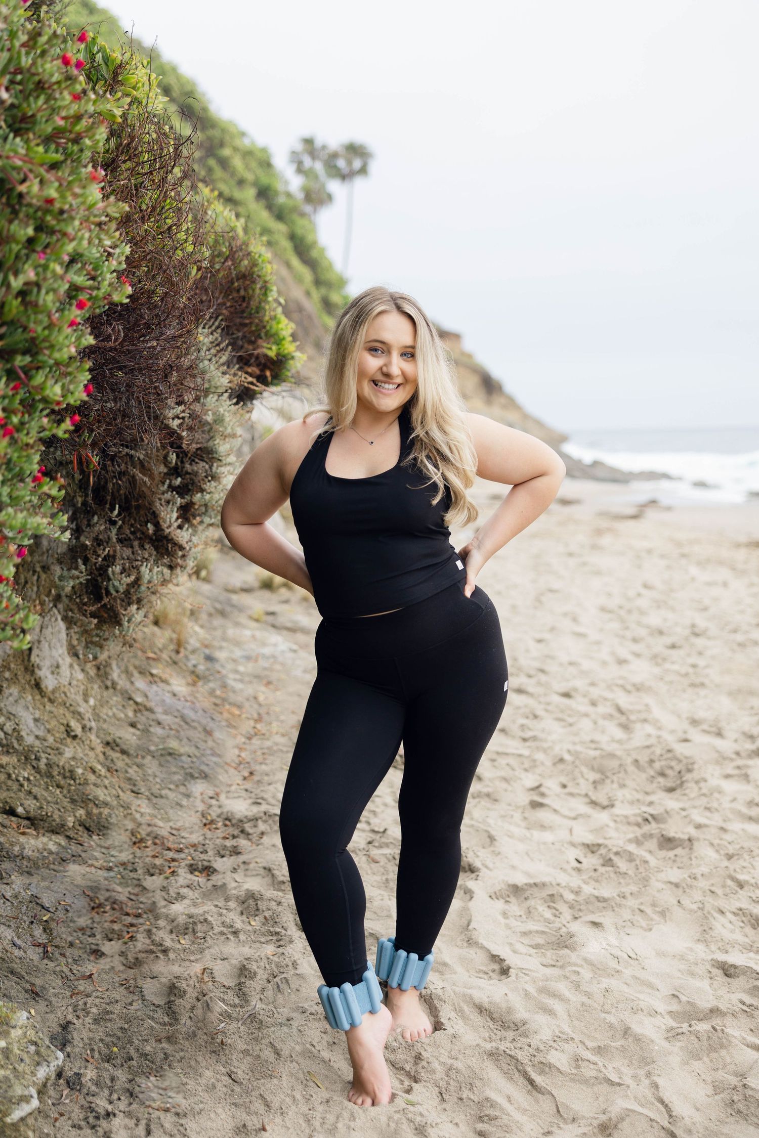 A person in athletic wear poses confidently on a coastal path with ocean views.
