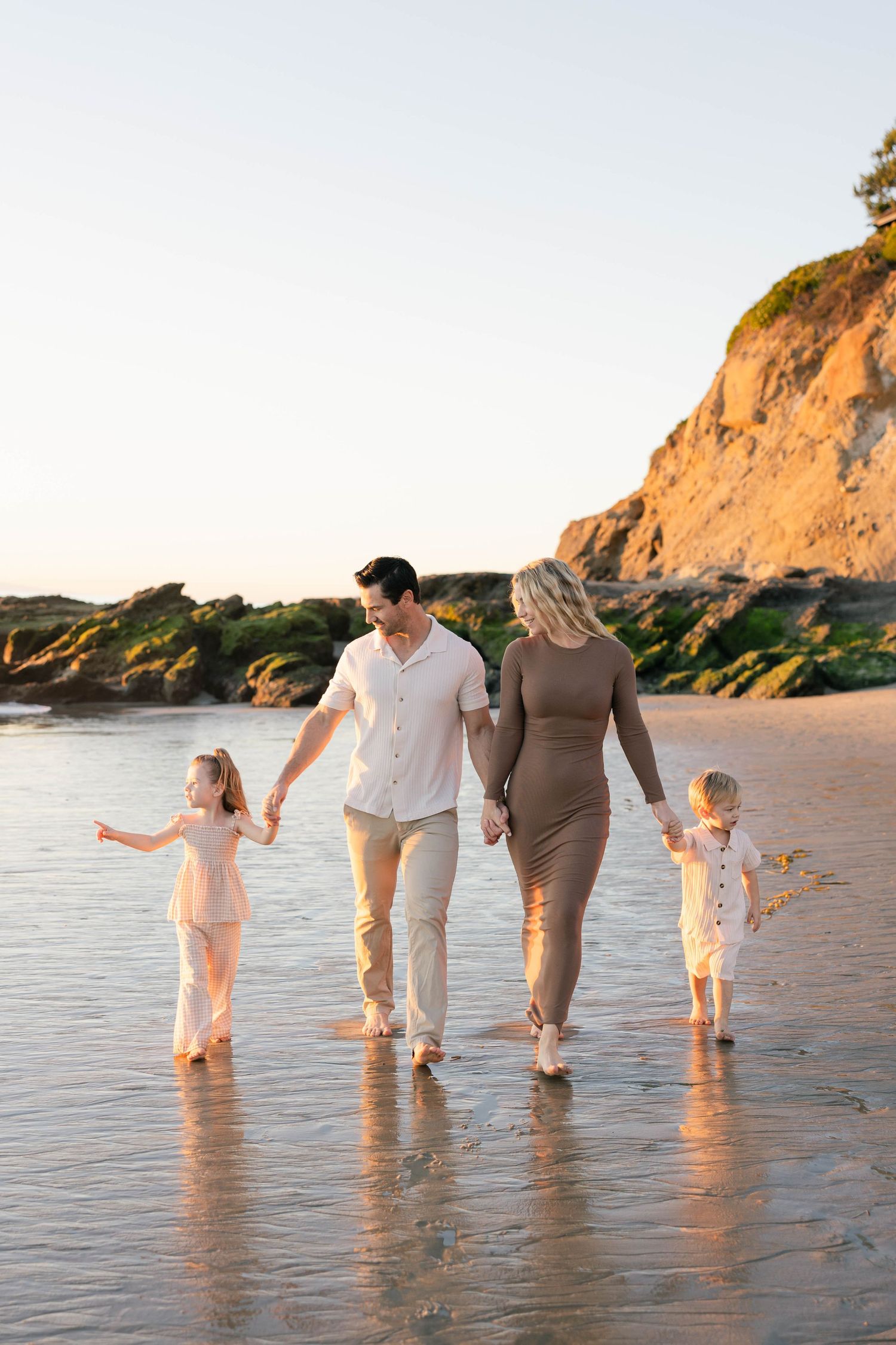Family walking together along the shoreline at sunset near coastal cliffs.