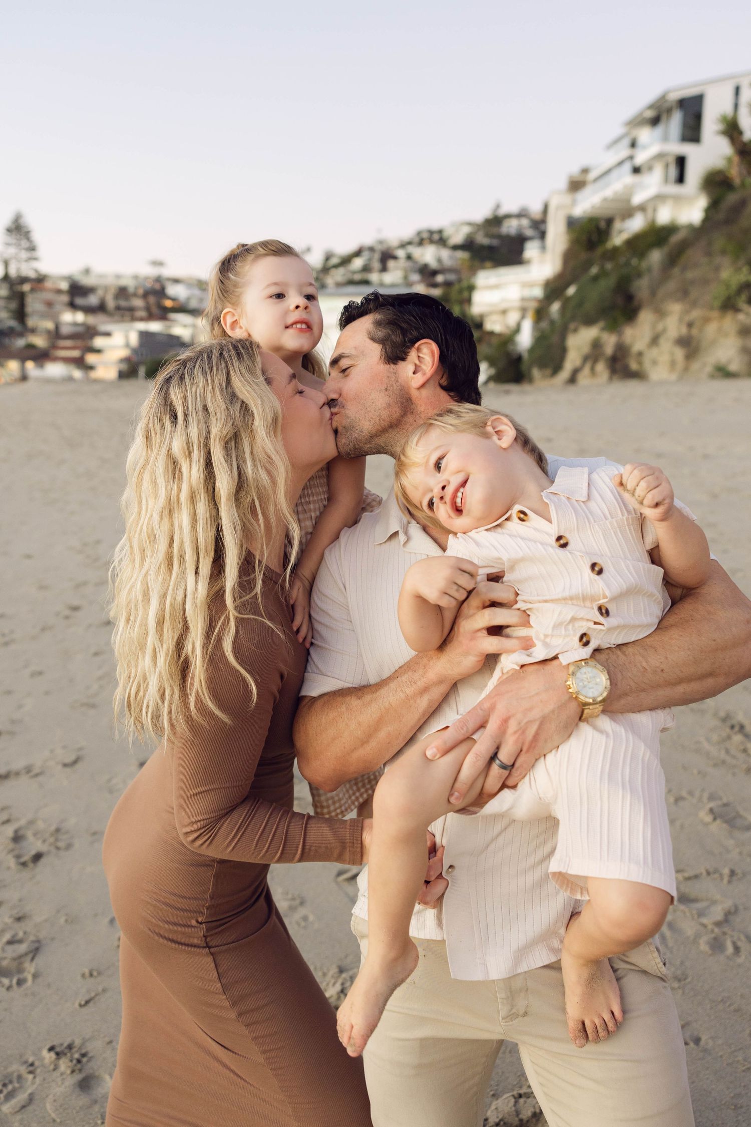 An intimate family portrait on the beach with coastal homes visible in the background.