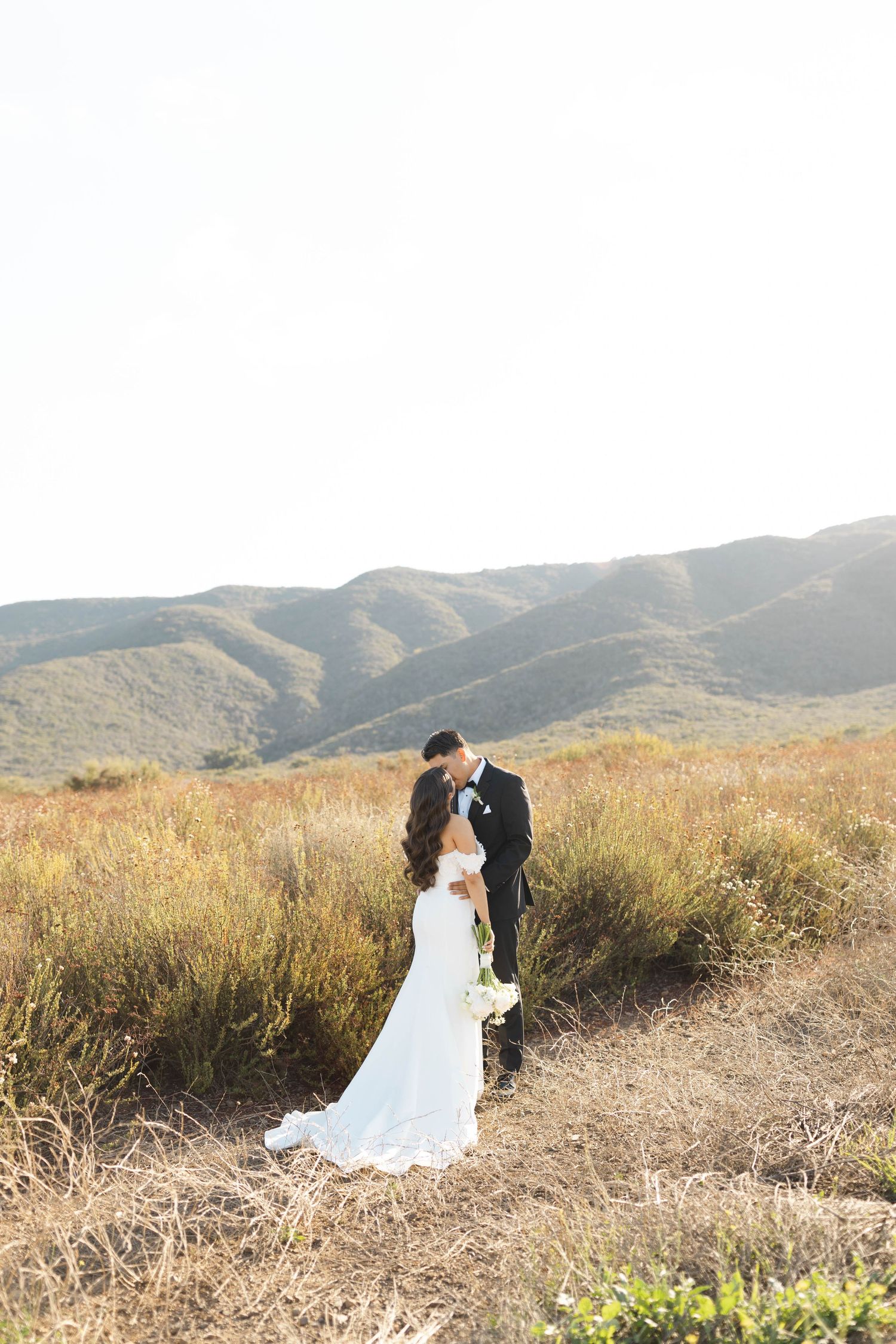 A romantic wedding photoshoot against rolling hills and golden grass at sunset.