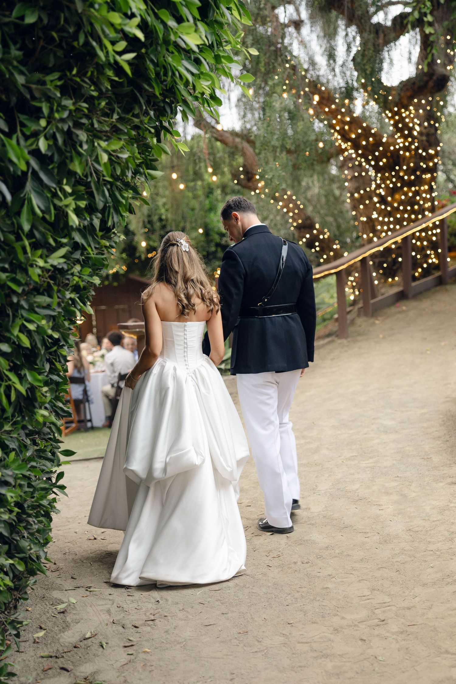 Couple walking along a garden path decorated with twinkling string lights overhead.