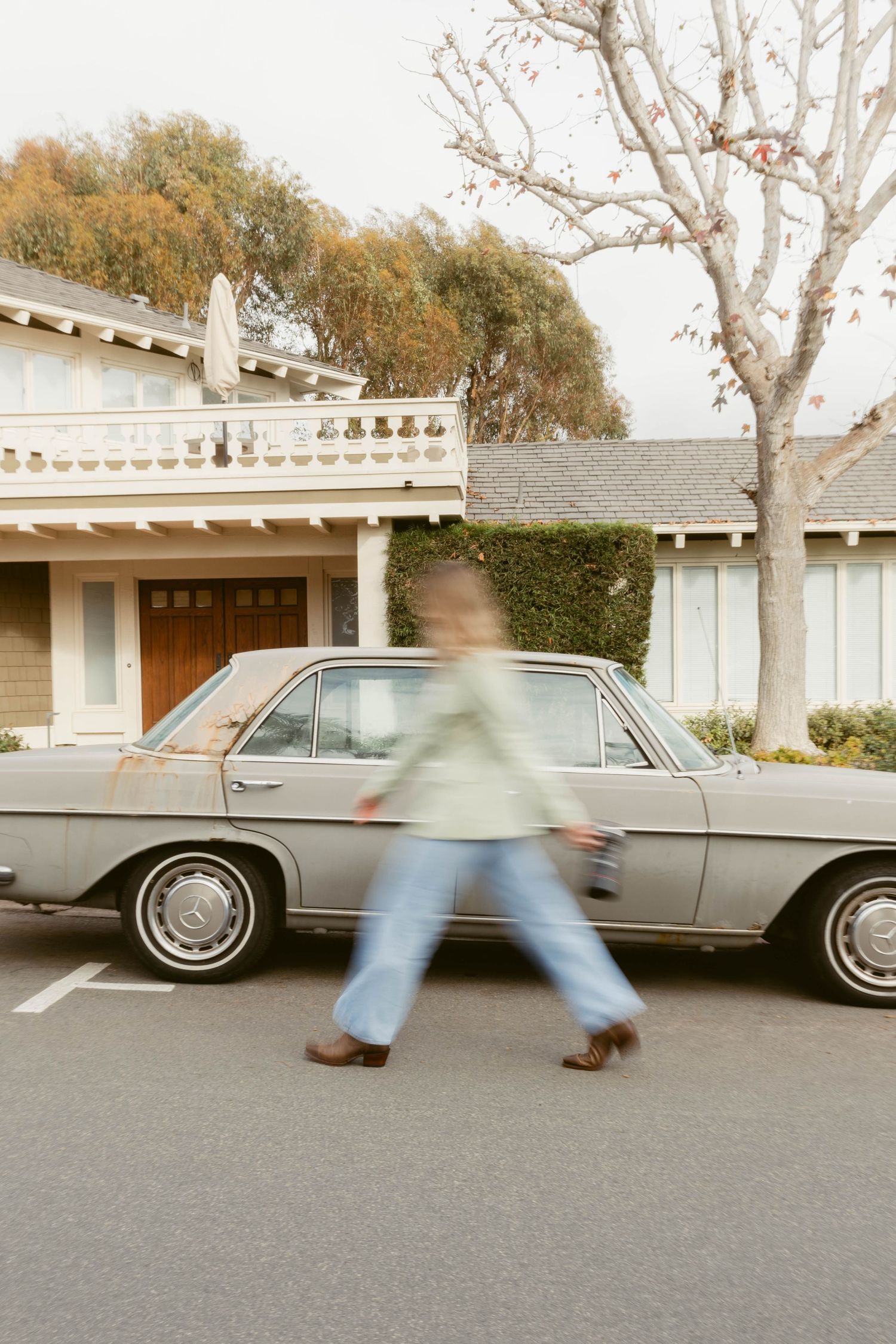 Vintage car parked in front of house with motion blur of someone walking past.