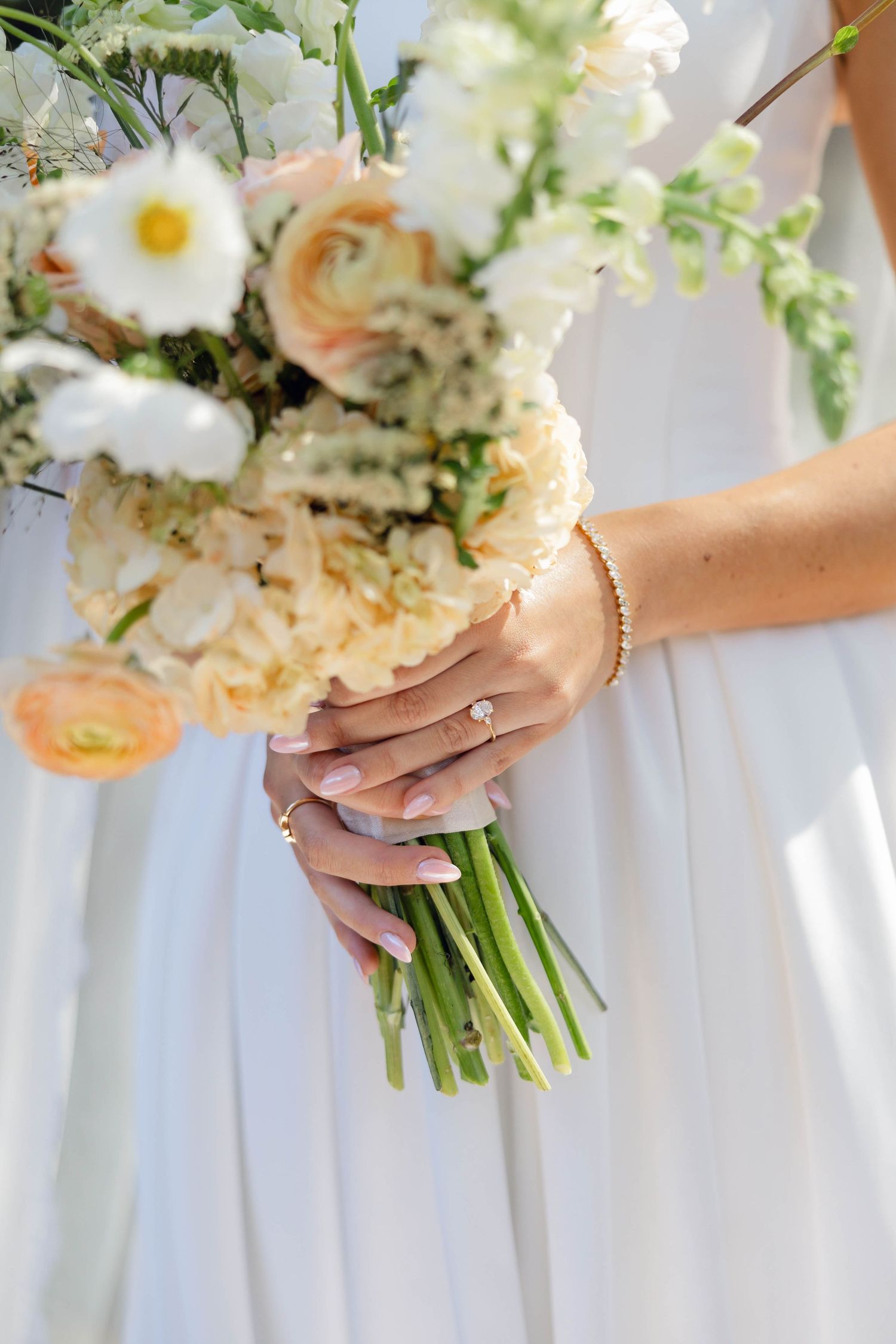 Wedding bouquets with white flowers and greenery held by bridesmaids in a row.