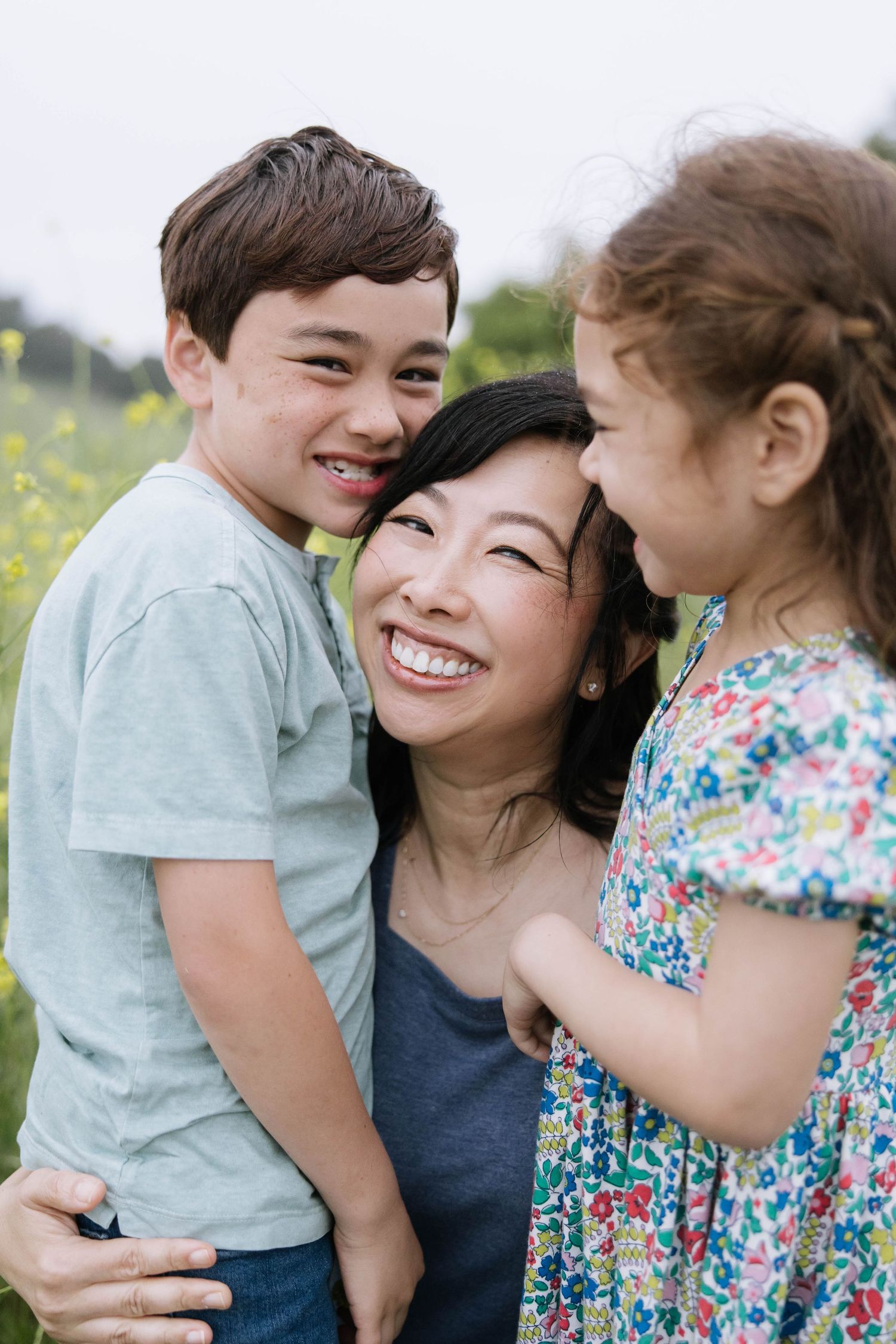 Family shares joyful laughs and cuddles in a sunny meadow filled with wildflowers.