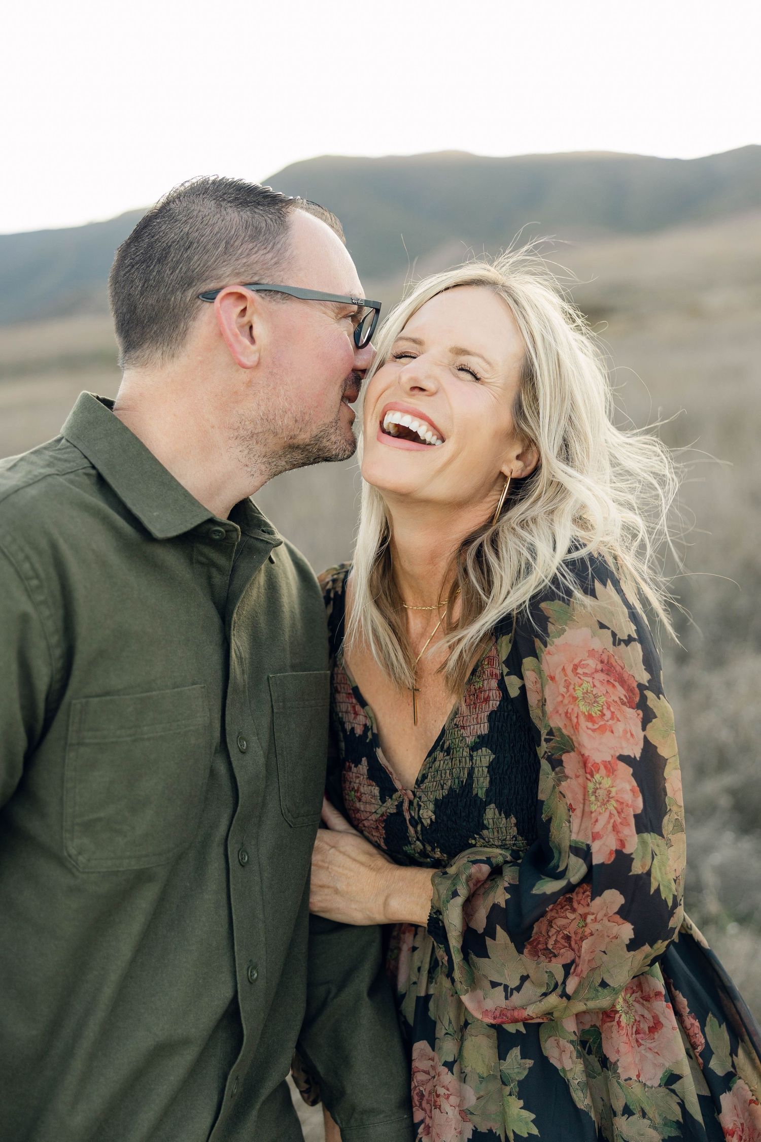 Candid moment of laughter between couple against mountain backdrop.