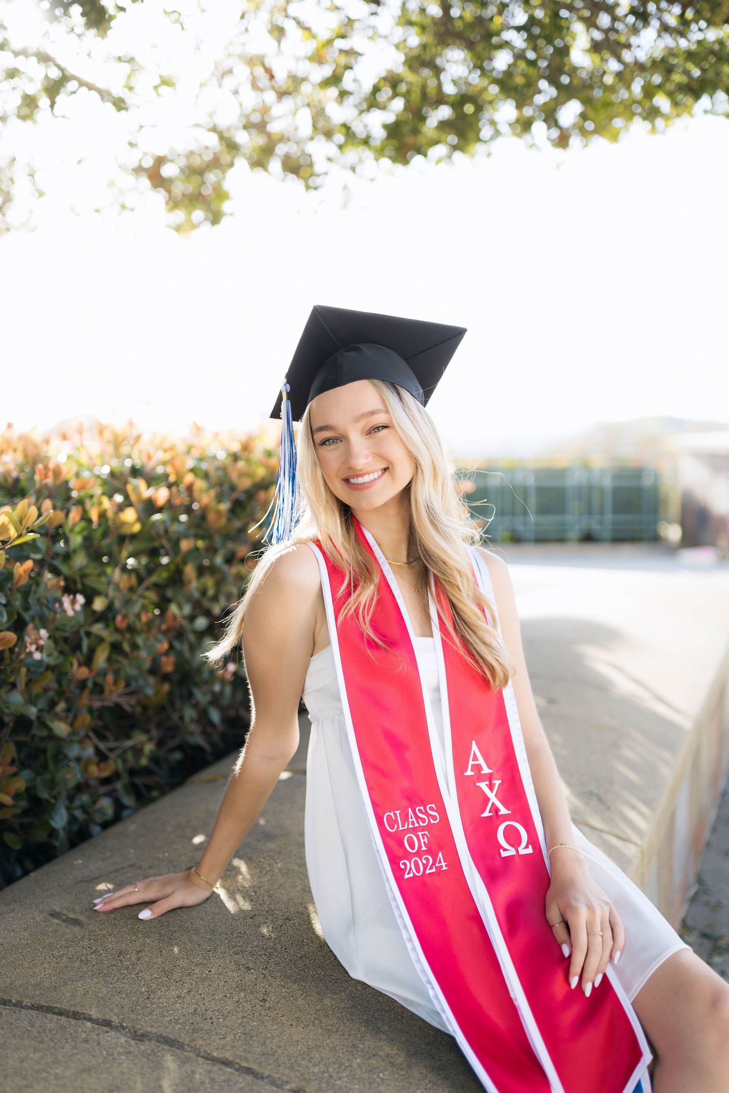 Graduate in cap and red stole poses outdoors for commemorative photos.