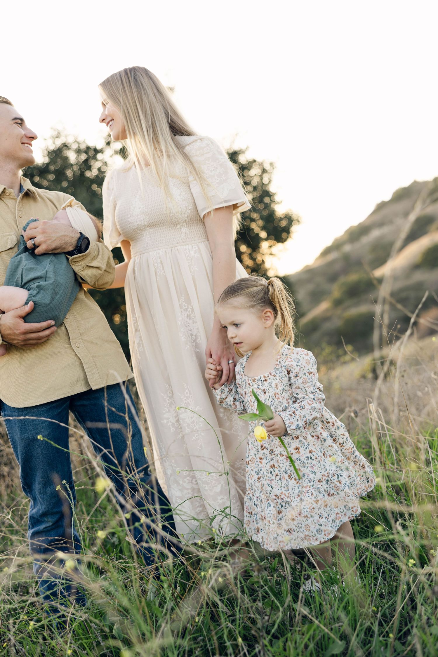 A family in light colored outfits poses together in a grassy field at sunset.